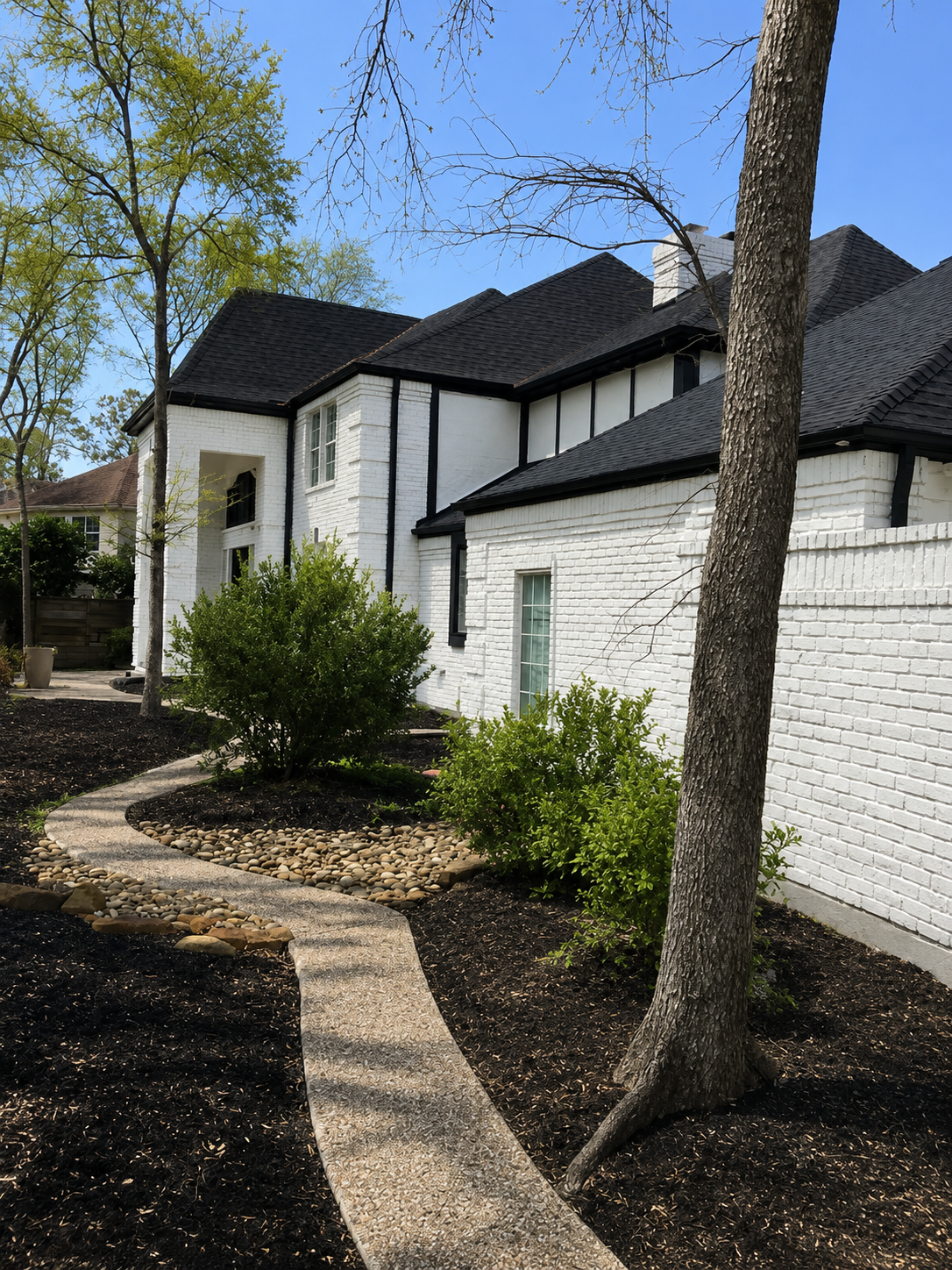 White stucco house with black roof, curved stone walkway, and trees in the front yard
