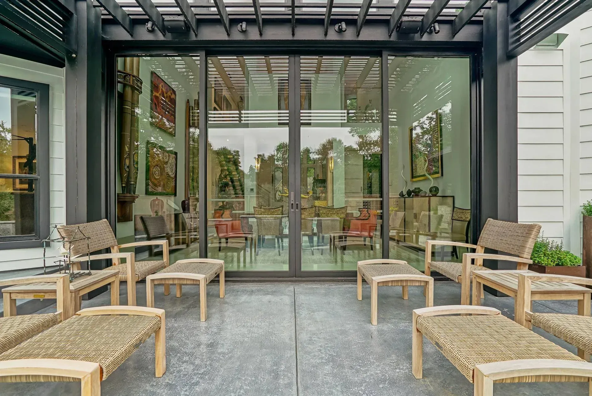 Covered patio seating area with wicker chairs facing glass doors and a modern indoor-outdoor space
