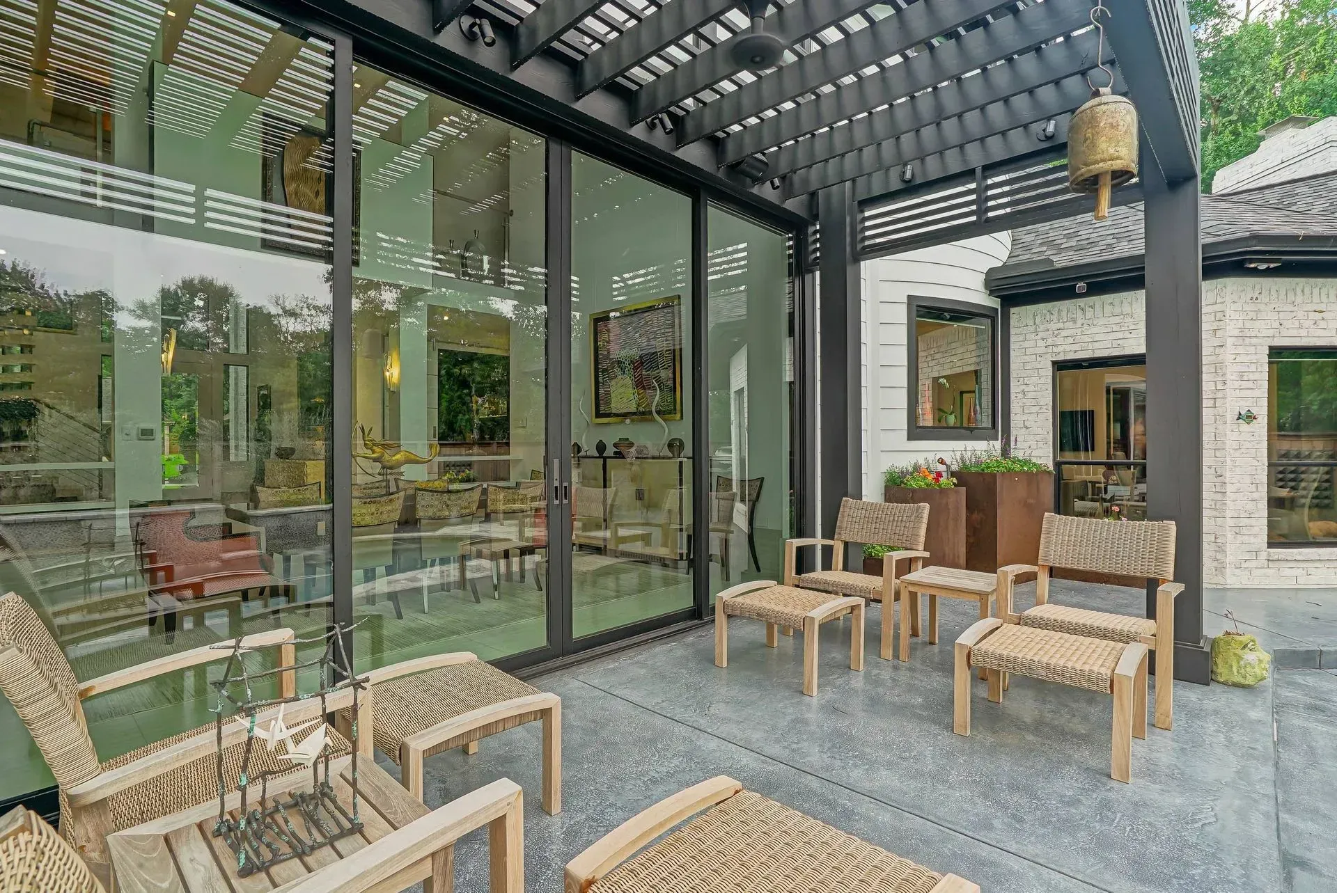 Modern patio seating area with wicker chairs, glass walls, and a metal pergola ceiling