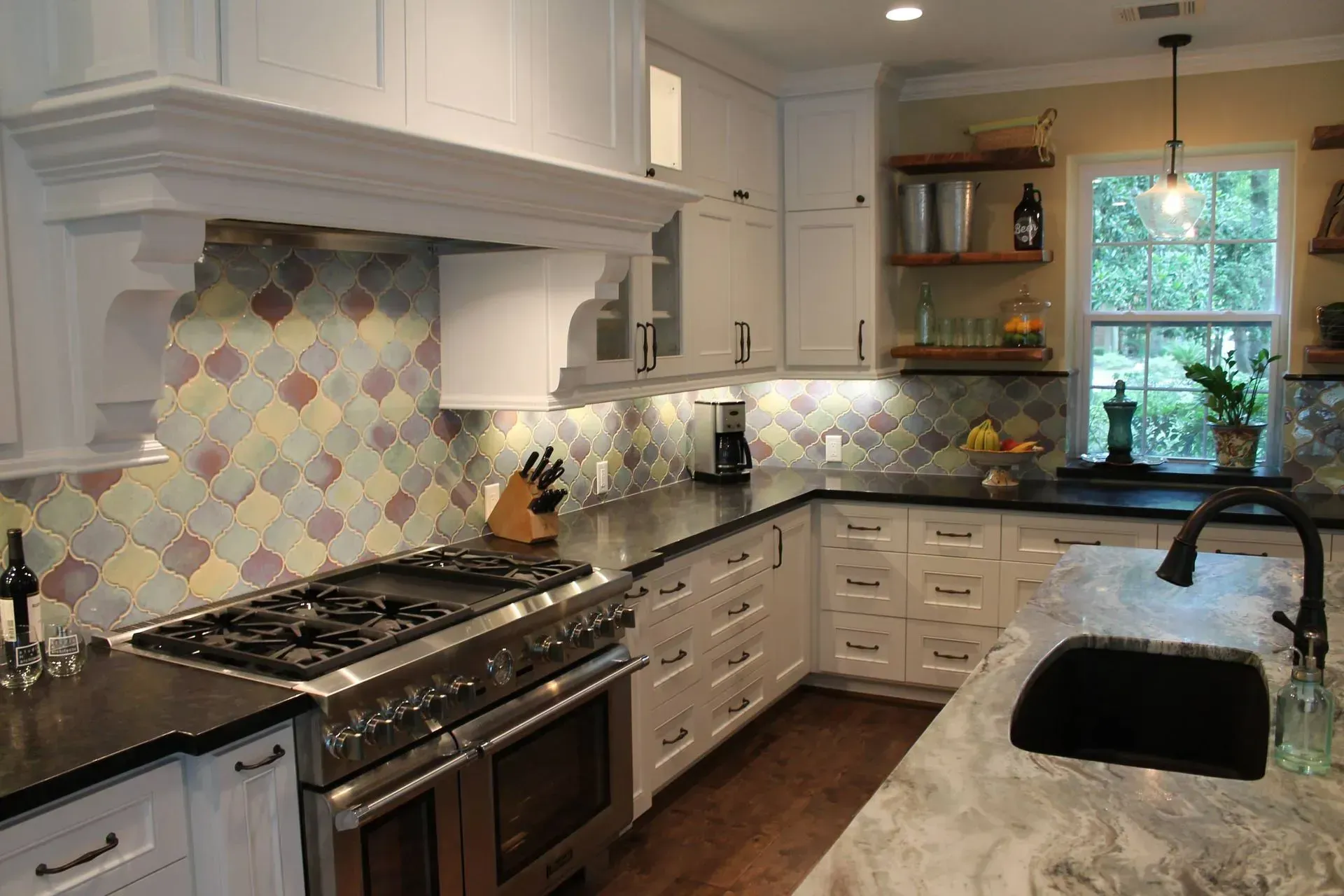 Bright kitchen with white cabinets, multicolor tile backsplash, granite counters, and a window over the sink.