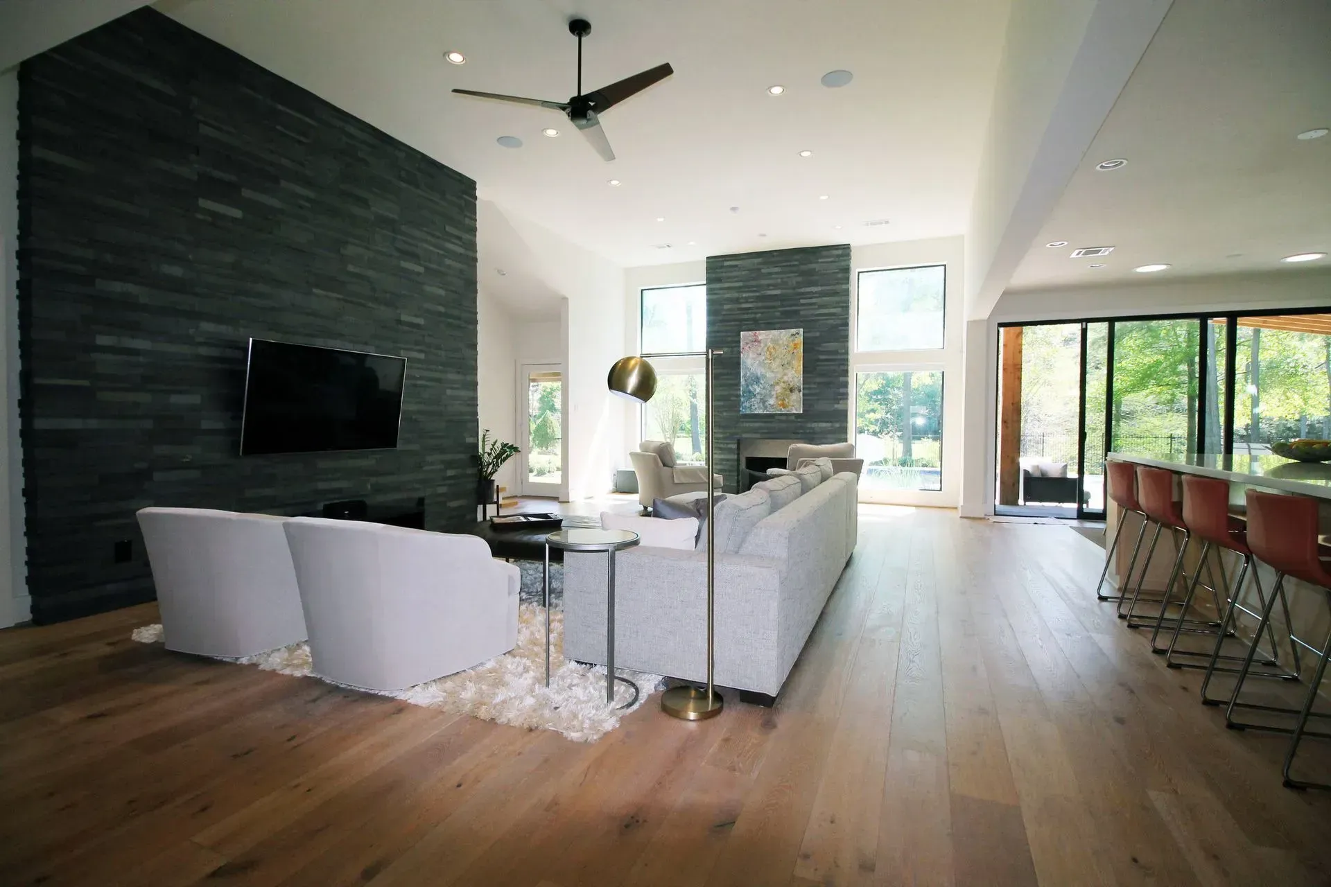 Modern open-plan living room with white sofas, wood floors, wall-mounted TV, and large windows