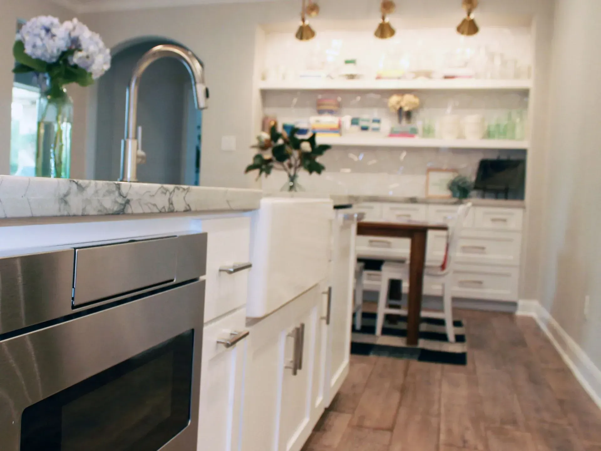 Modern kitchen with white cabinets, marble island, stainless oven, wood floors, and gold pendant lights