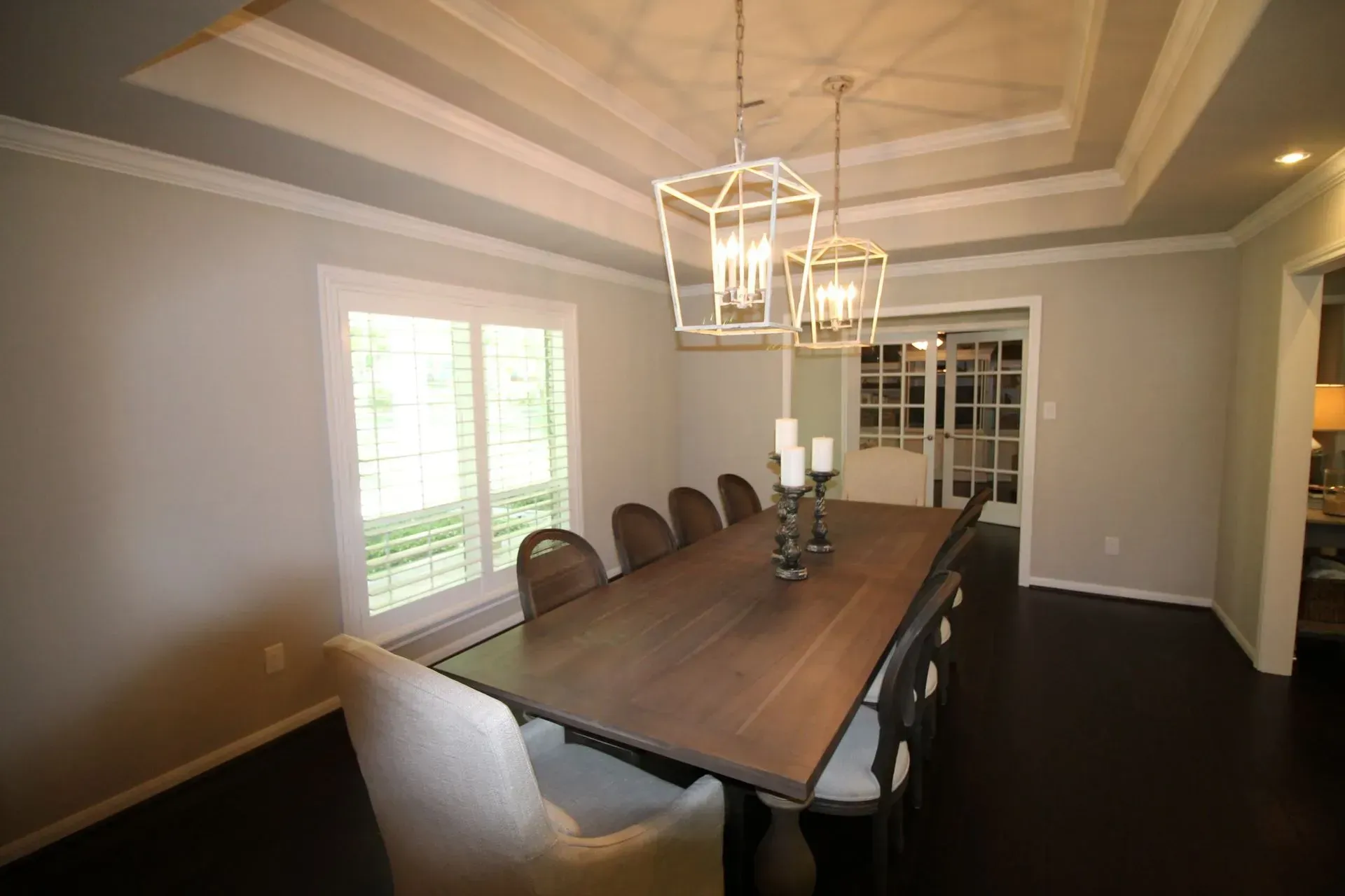 Formal dining room with long wooden table, chandelier, and white chairs under tray ceiling