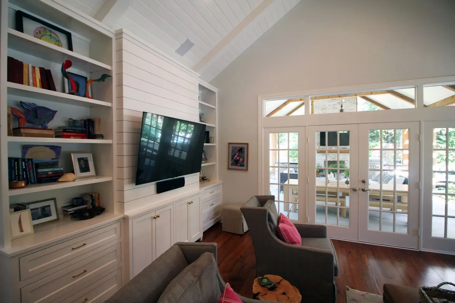 Bright living room with built-in shelves, wall-mounted TV, sofa, and French doors opening to a sunroom