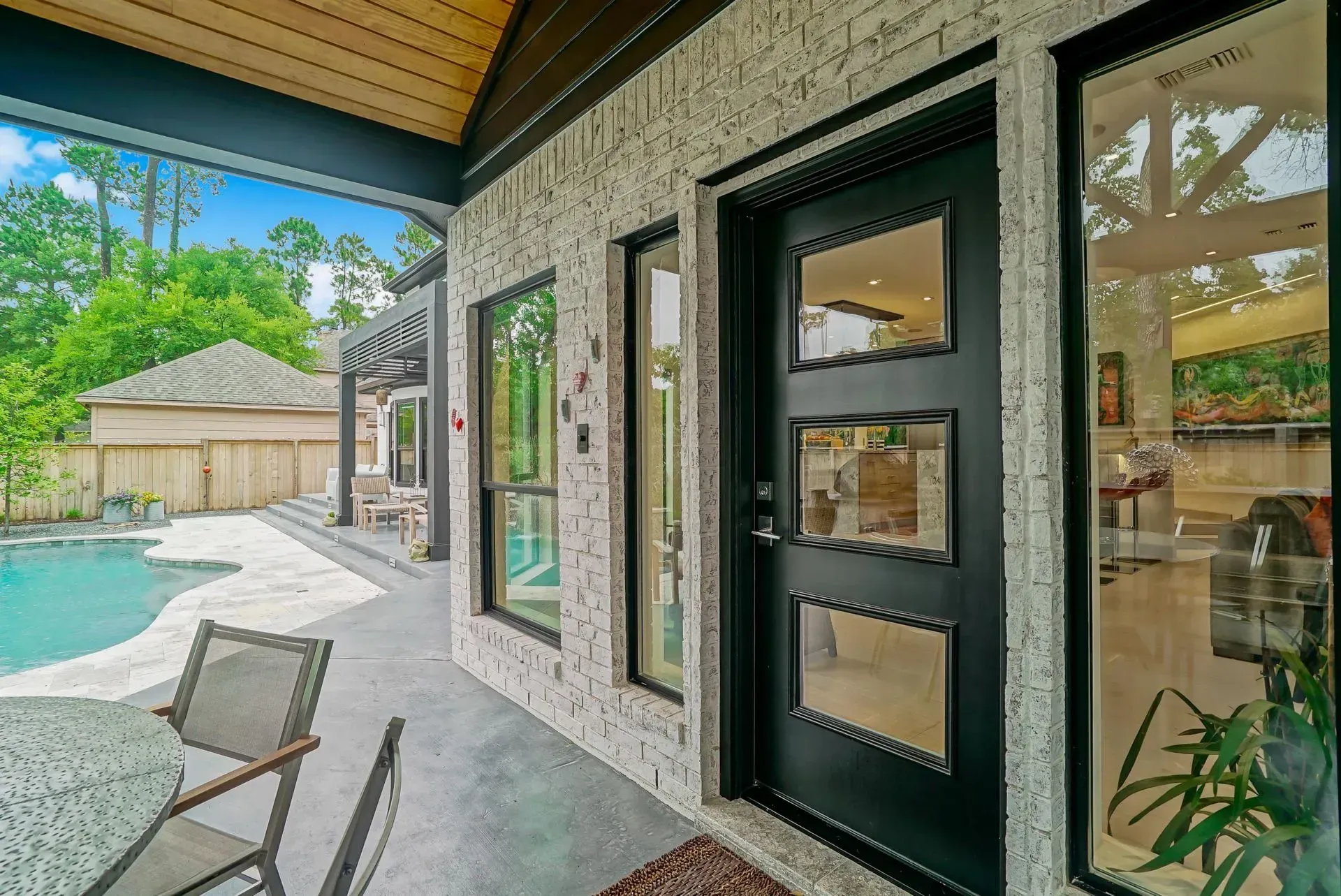Covered patio beside a pool, with black French doors, wicker chairs, and a stone exterior wall