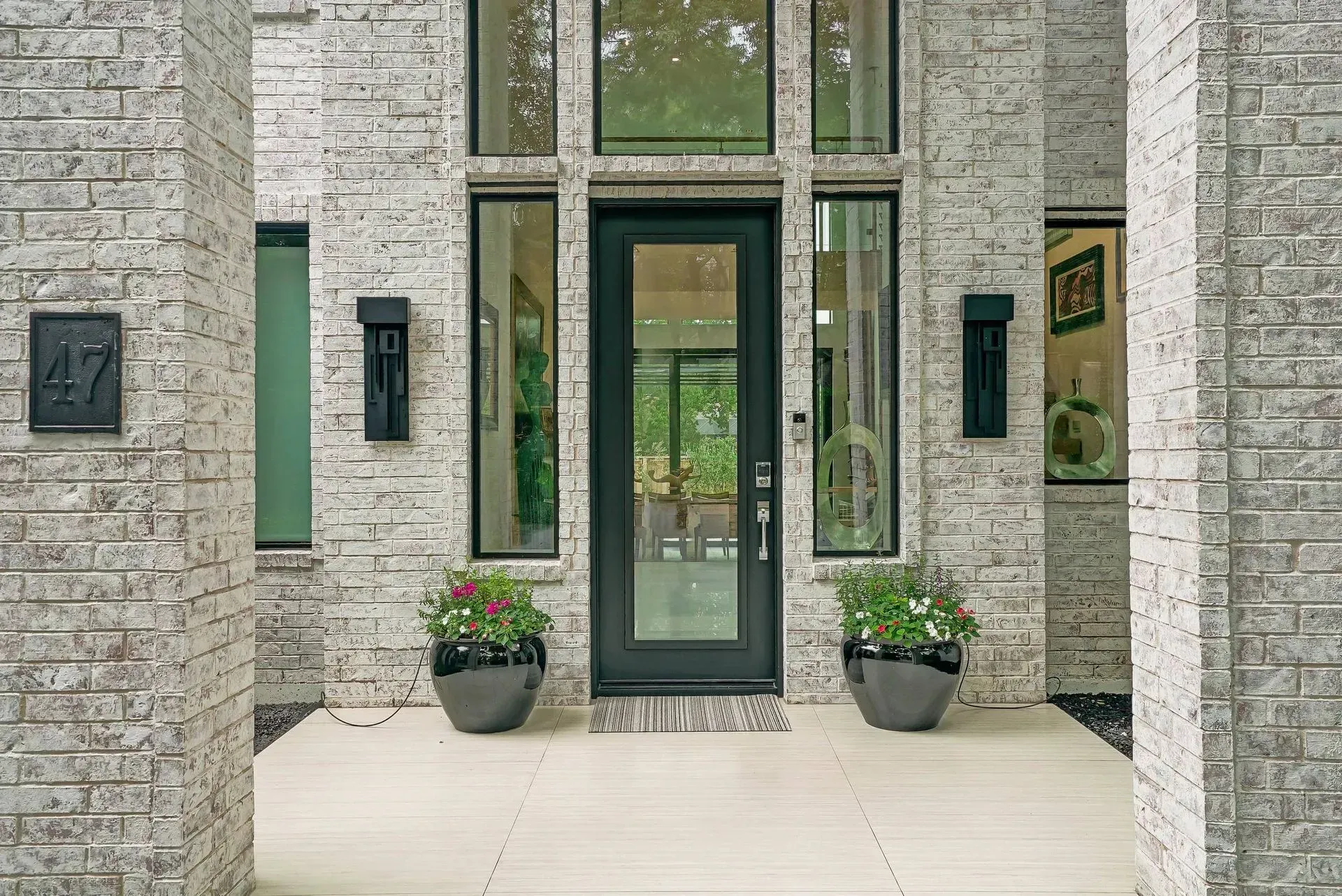Modern stone house entrance with black-framed glass door and potted plants on either side
