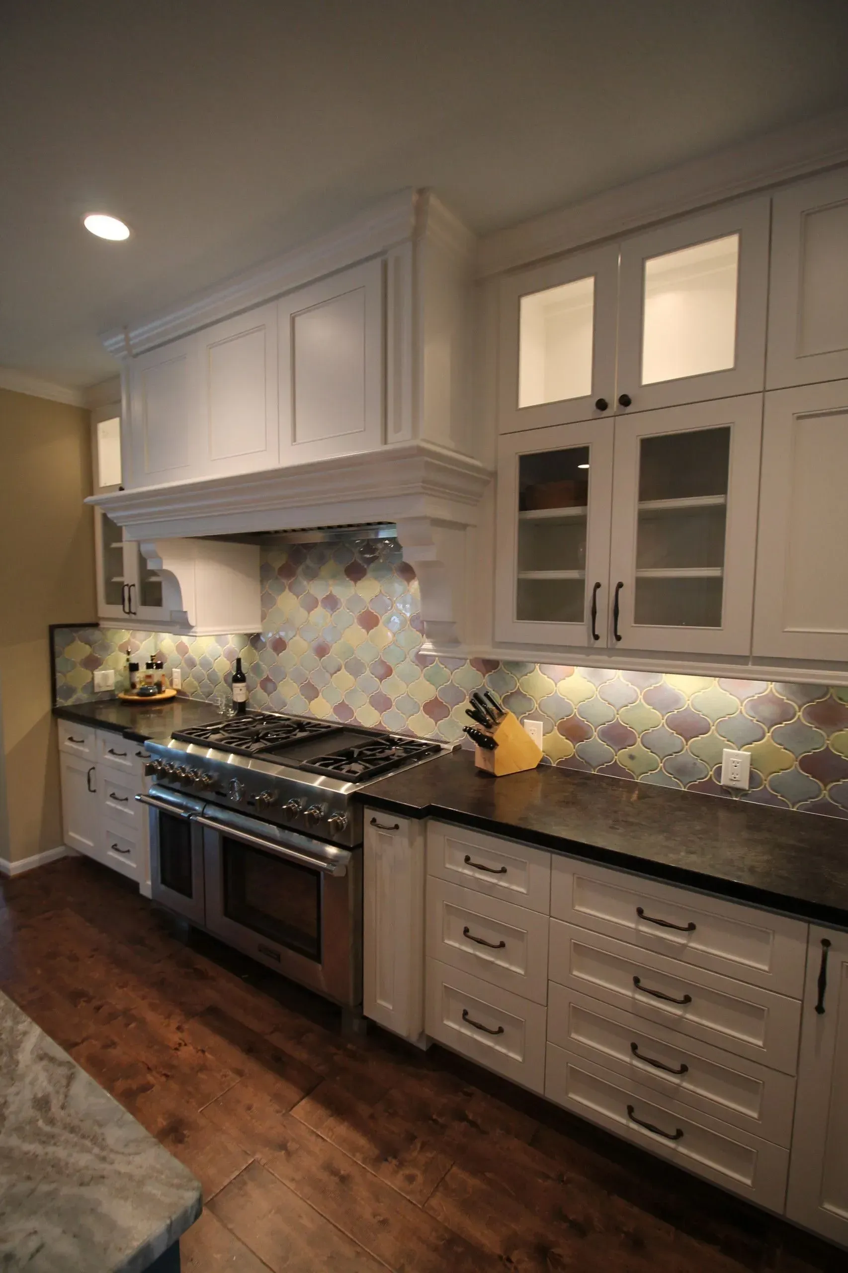 Modern kitchen with white cabinets, stainless stove, mosaic tile backsplash, and dark wood floor
