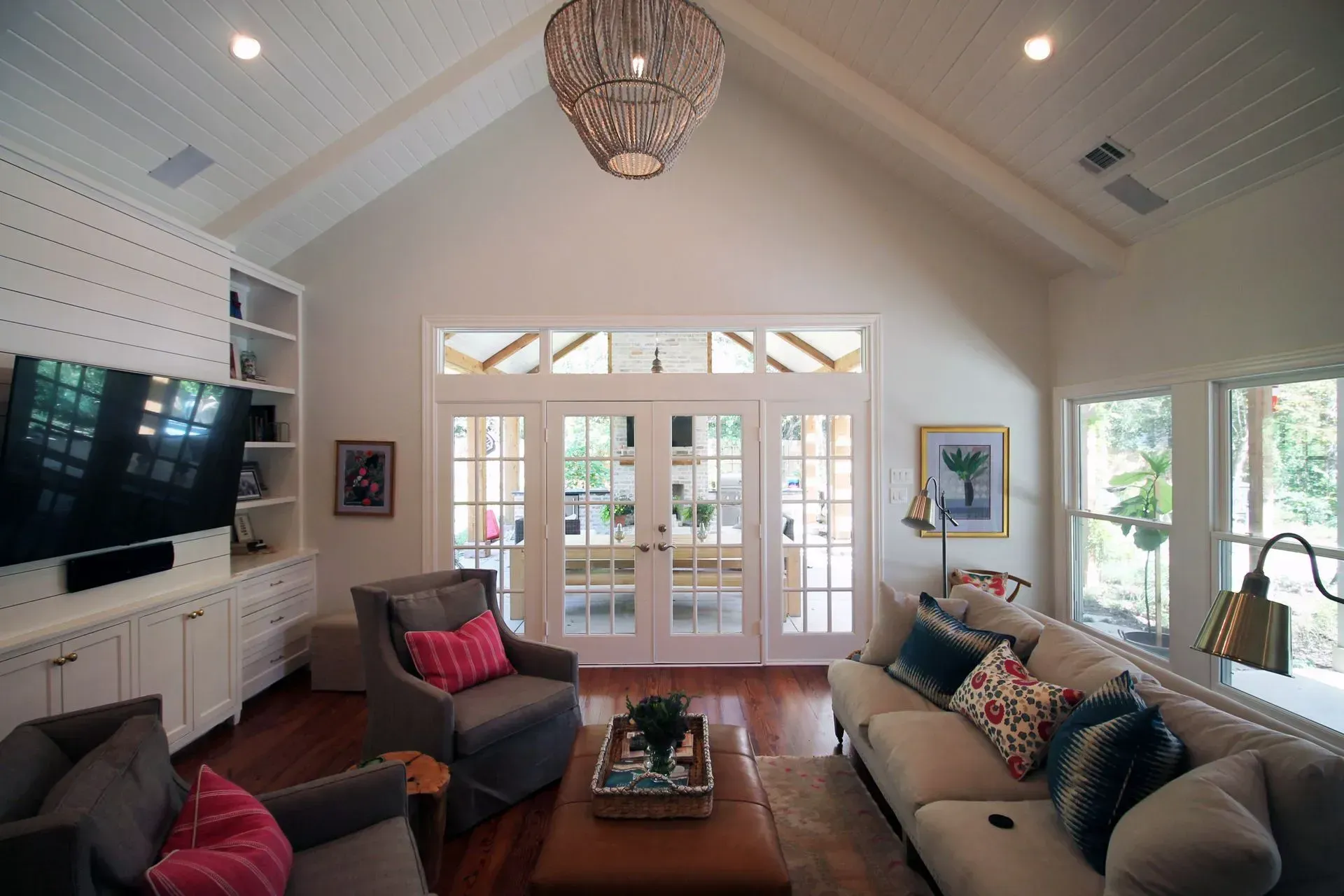 Bright living room with vaulted ceiling, sofas, TV, coffee table, and glass doors to a sunny patio.