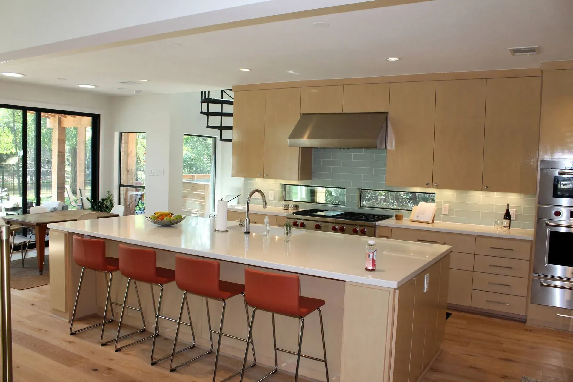 Modern kitchen with island, orange bar stools, light wood cabinets, and large windows