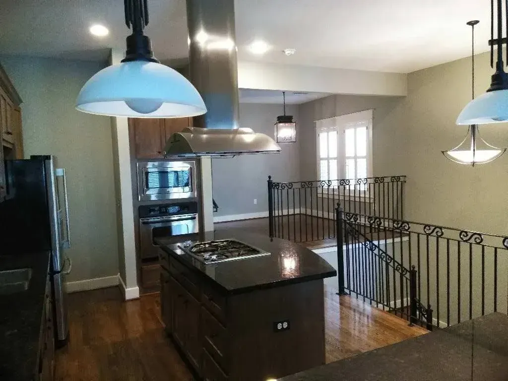Modern kitchen with black island, stainless steel appliances, pendant lights, and staircase railing view
