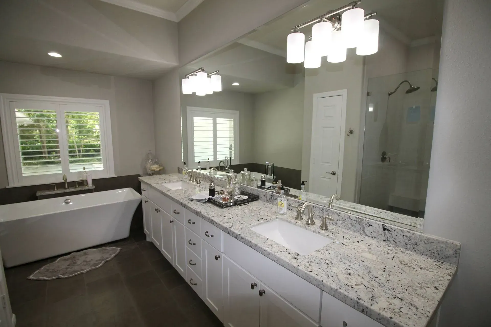 Modern bathroom with double vanity, large mirror, soaking tub, and white cabinets with granite countertops