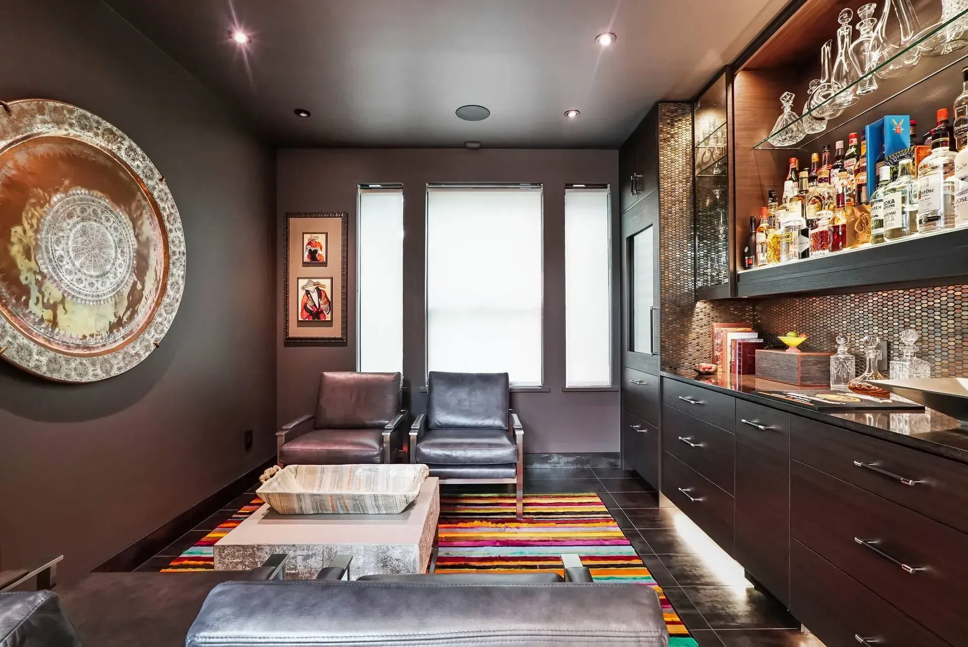 Modern lounge with dark walls, glass display shelves, colorful rug, and sleek seating near bright windows