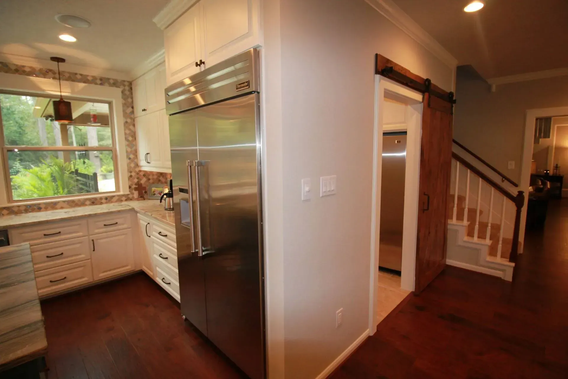 Kitchen and hallway with stainless steel refrigerator, white cabinets, wood floors, and staircase beyond
