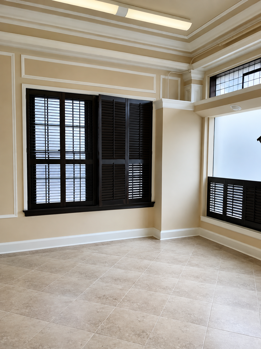 Empty beige room with black shuttered windows and cream trim, lit by daylight