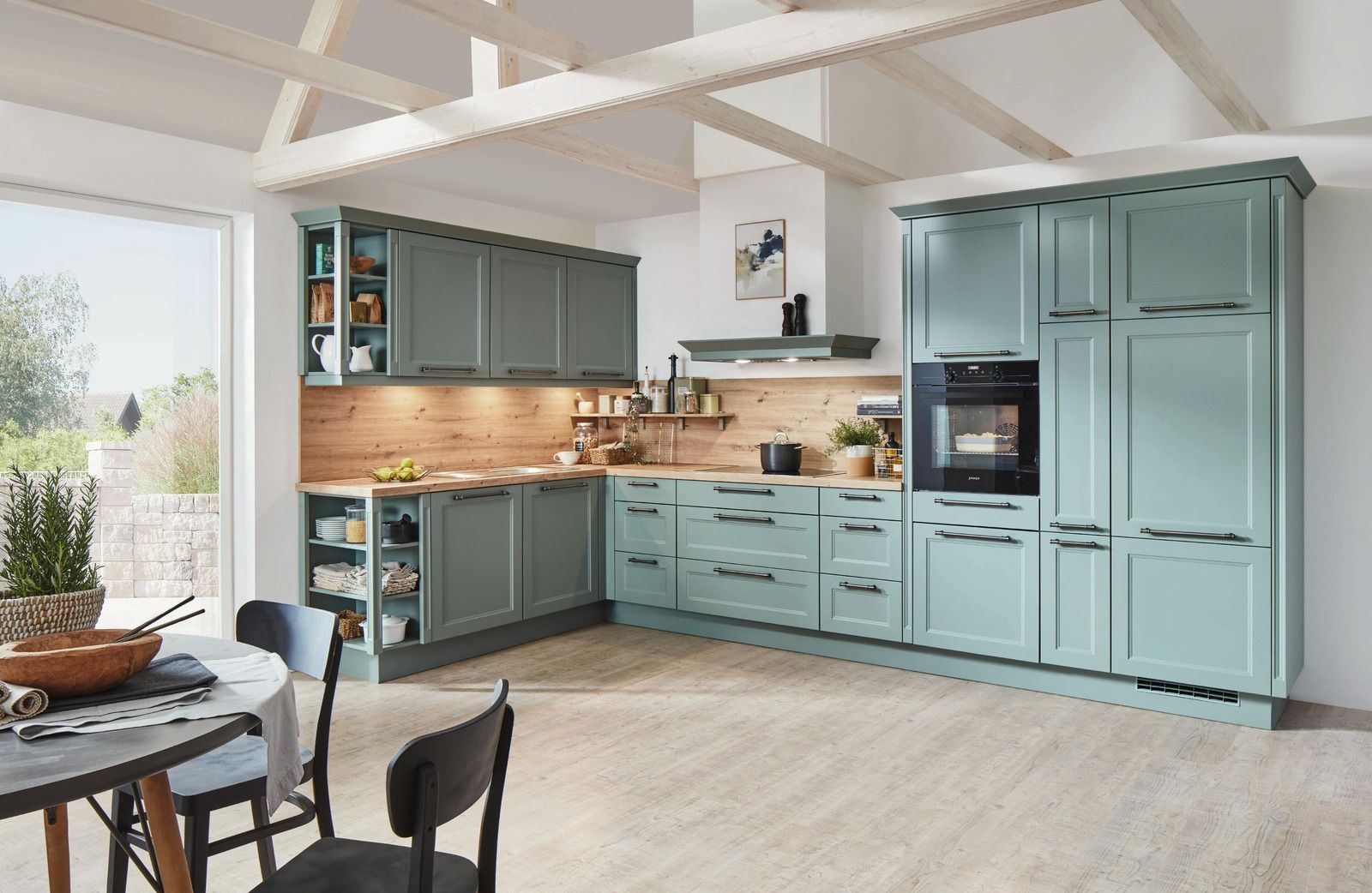 Bright modern kitchen with blue cabinets, wooden countertops, white beams, and a small dining table by the window