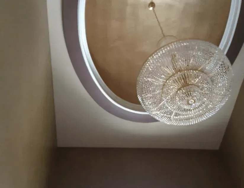 Ceiling with oval recessed detail and a hanging crystal chandelier against beige walls.