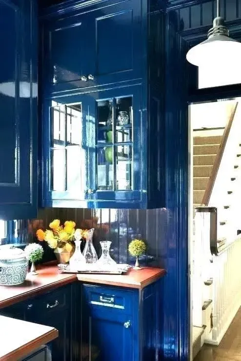 Blue kitchen with glossy cabinets, white countertops, fruit bowl, and a view of stairs through an open doorway
