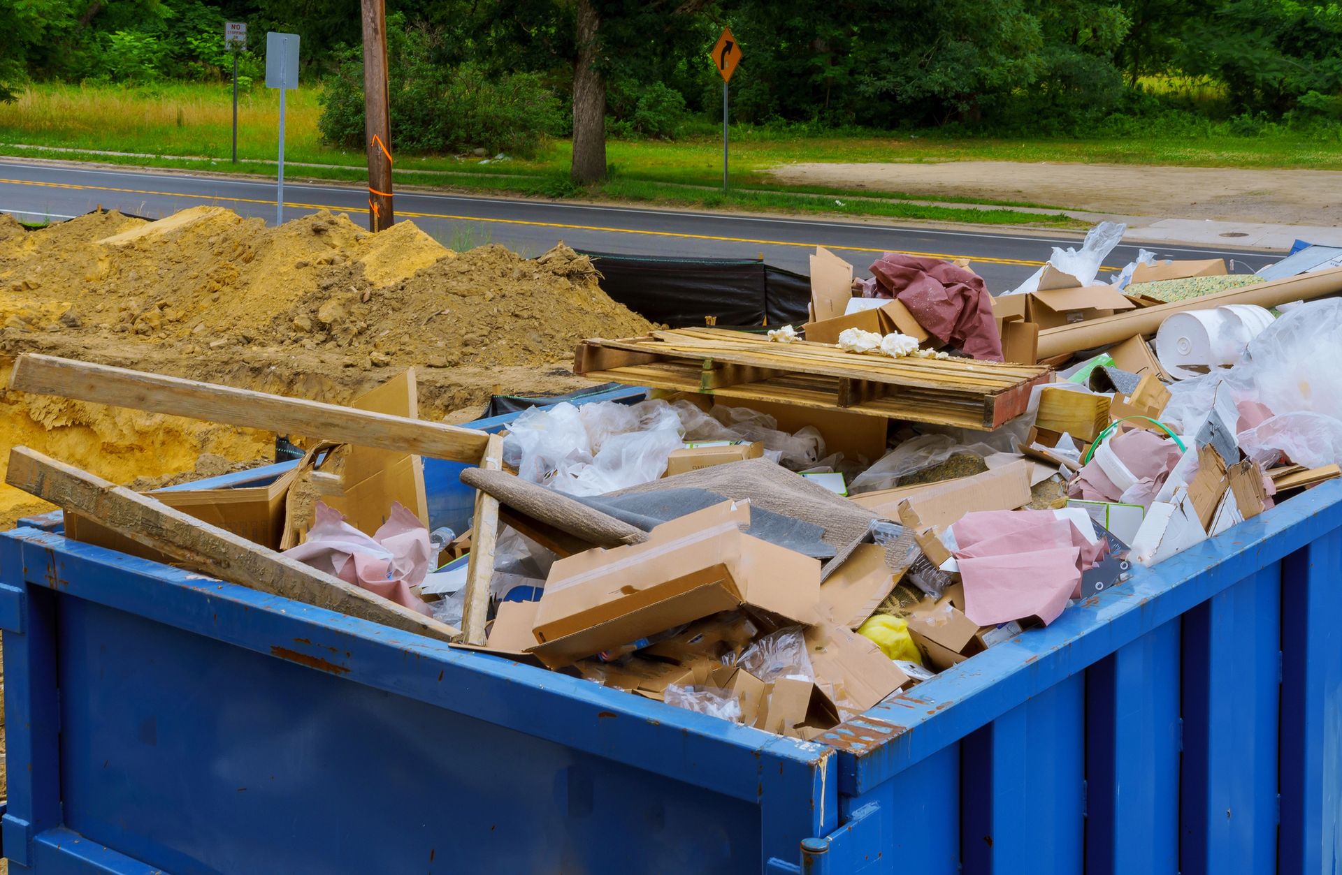 A blue dumpster filled with a lot of trash on the side of the road.