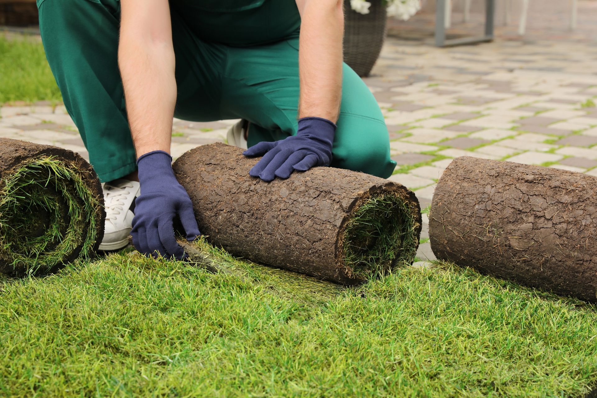 A man is rolling up rolls of turf on a patio.