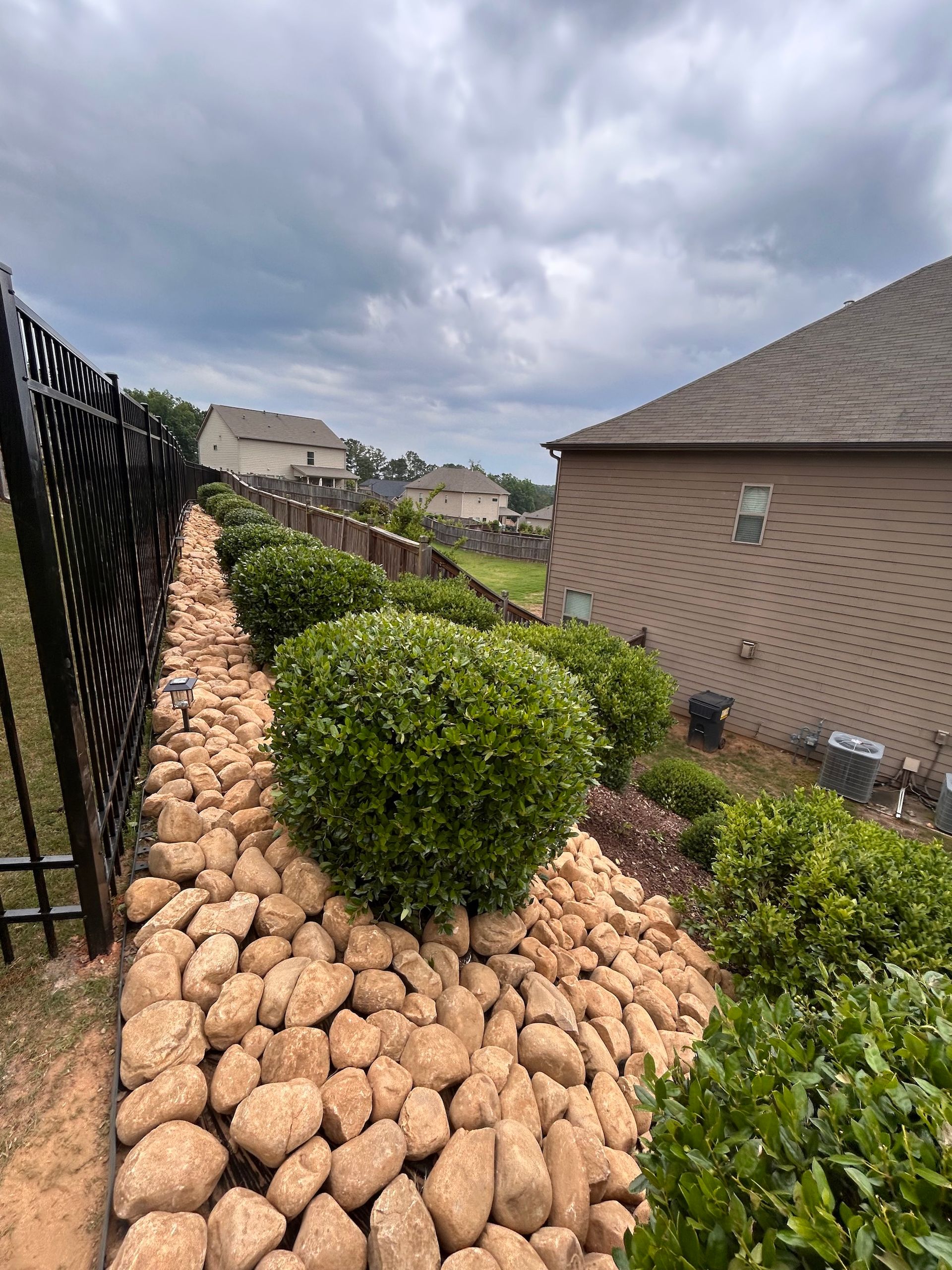 A house with a fence and a rock garden in front of it.