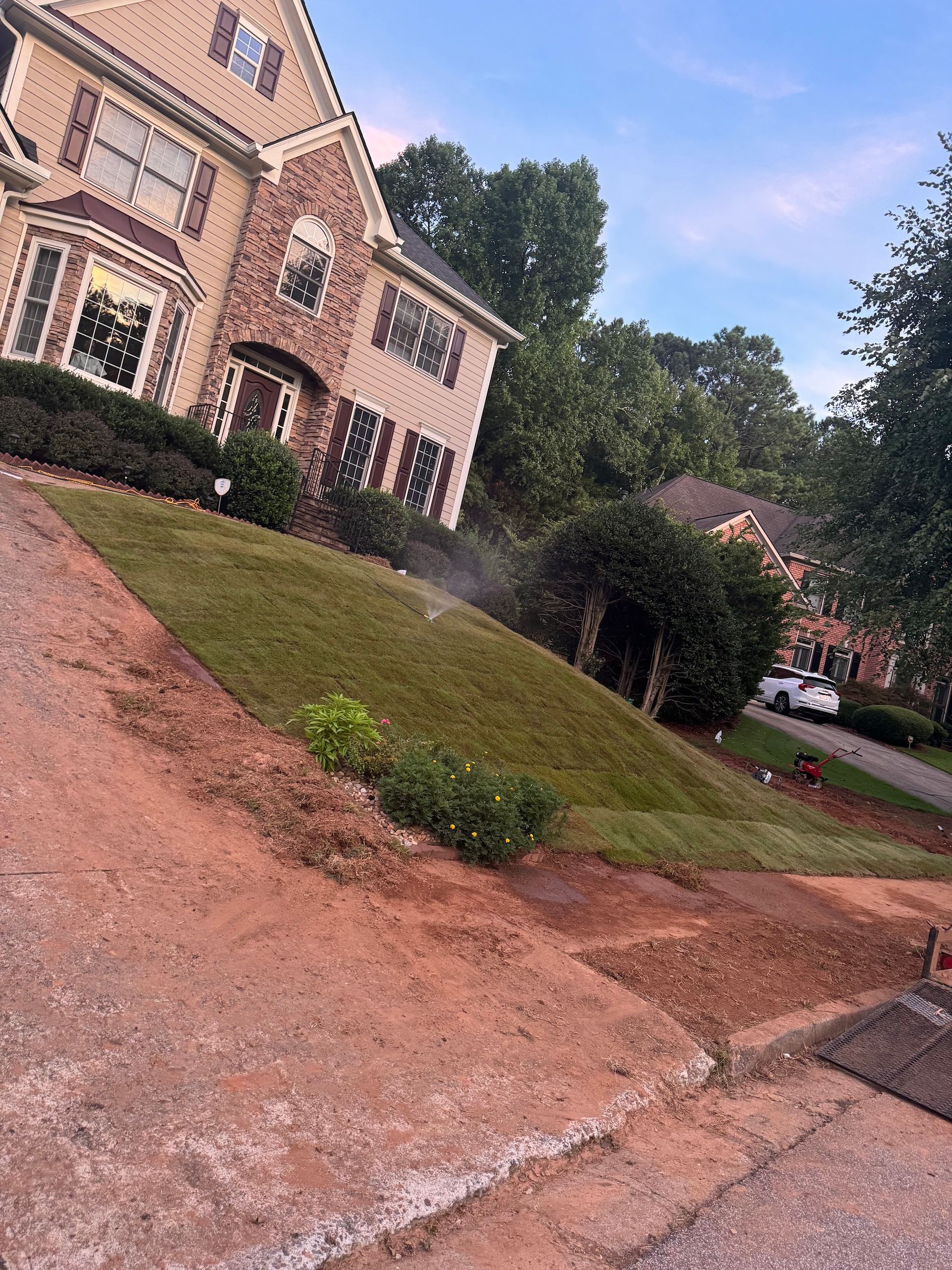 A large house is sitting on top of a hill next to a dirt road.