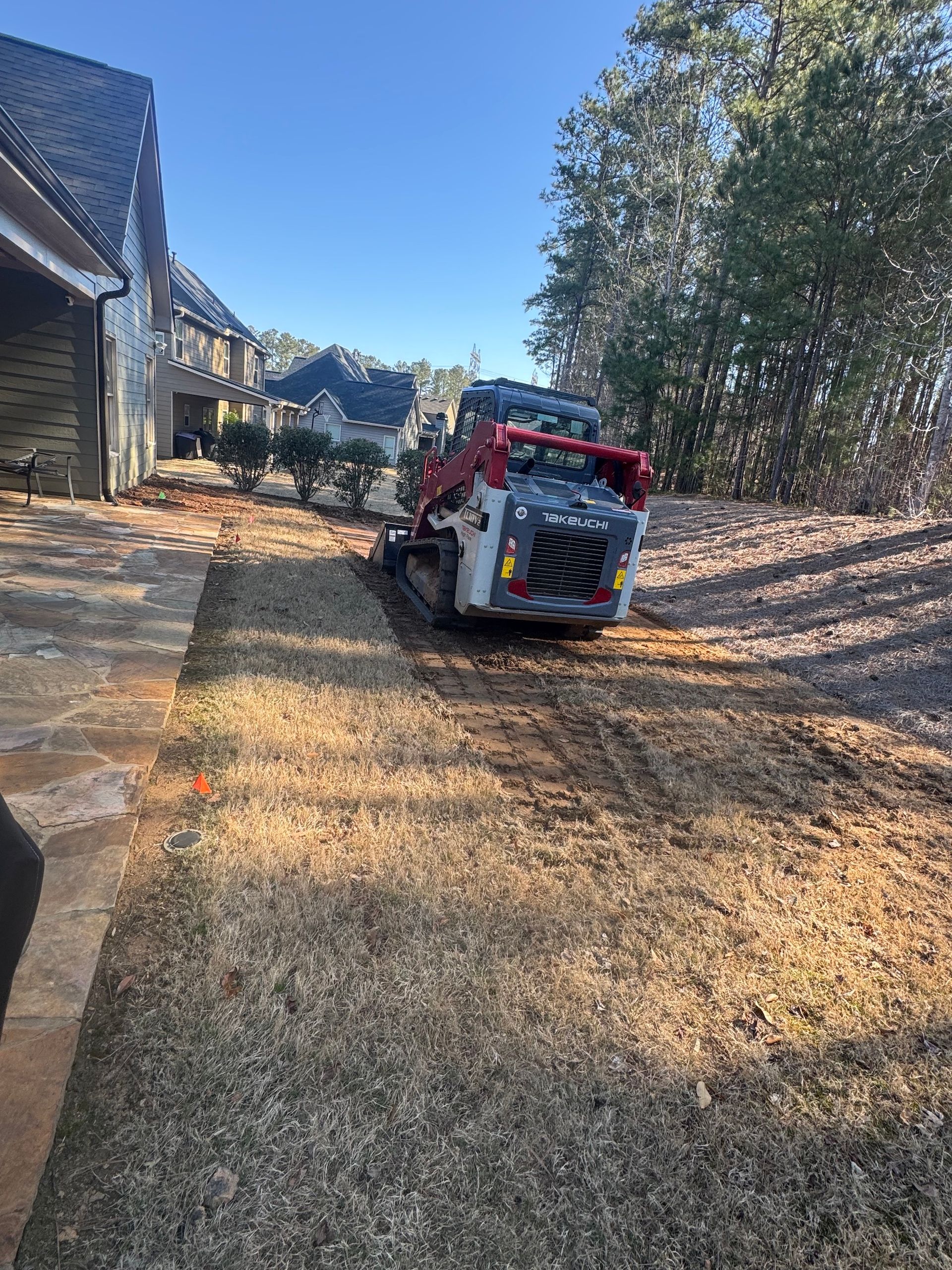 A bulldozer is driving down a dirt road in front of a house.
