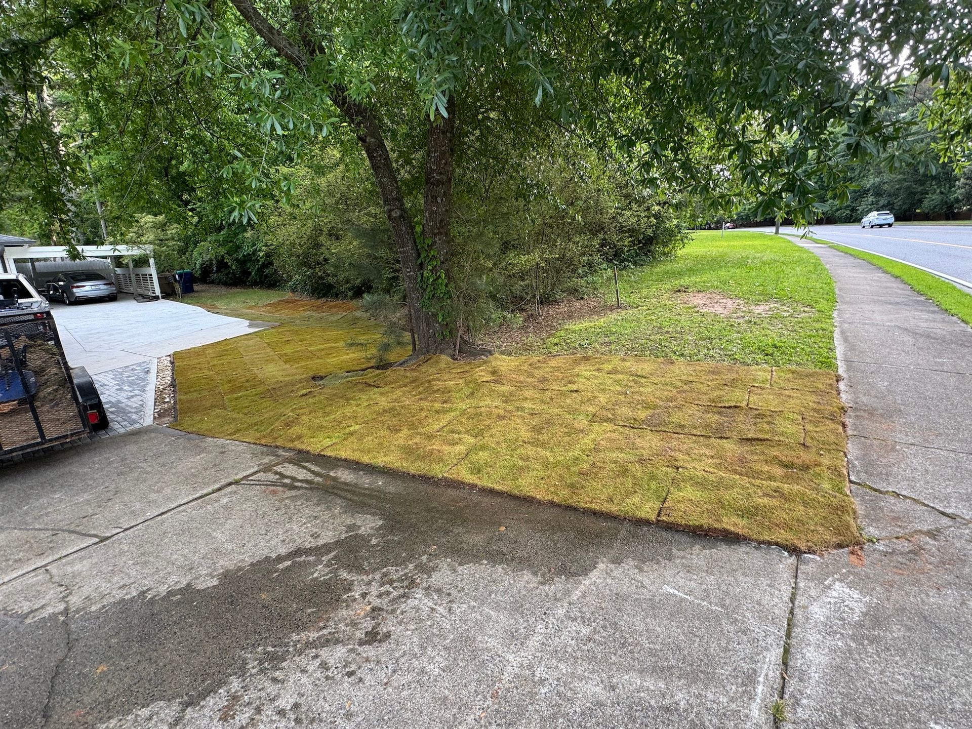 A trailer is parked on the side of the road next to a lush green lawn.