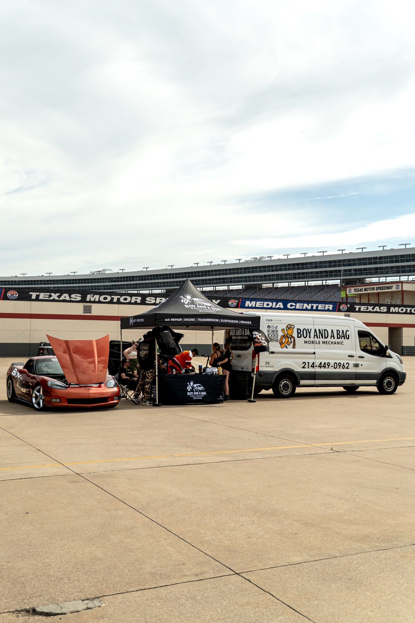 Race car with open hood and a white van on a track under cloudy skies
