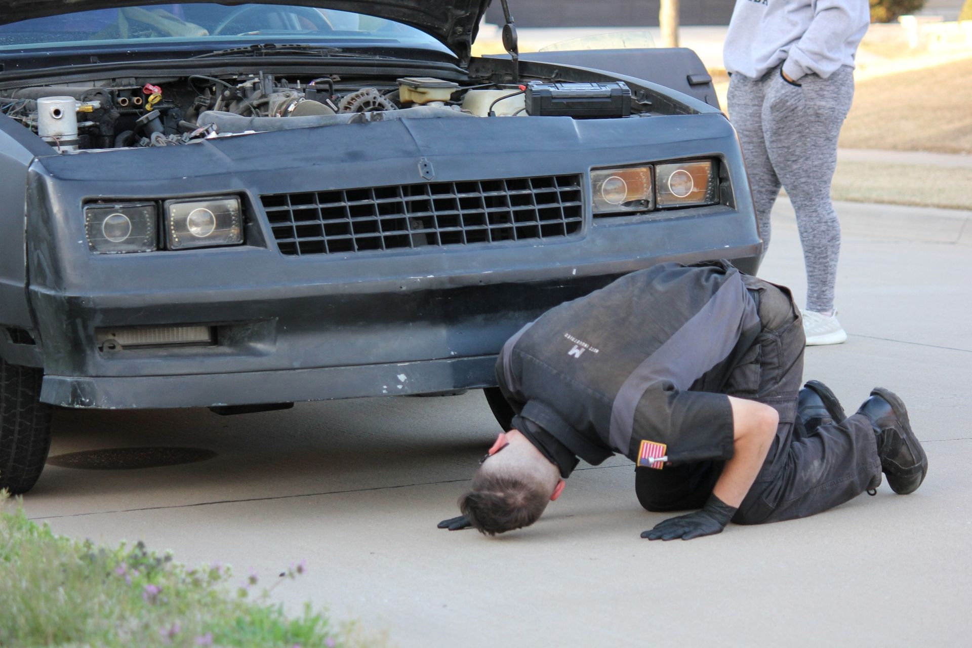 Police officer kneeling over a person on the pavement in front of a damaged car after an apparent crash