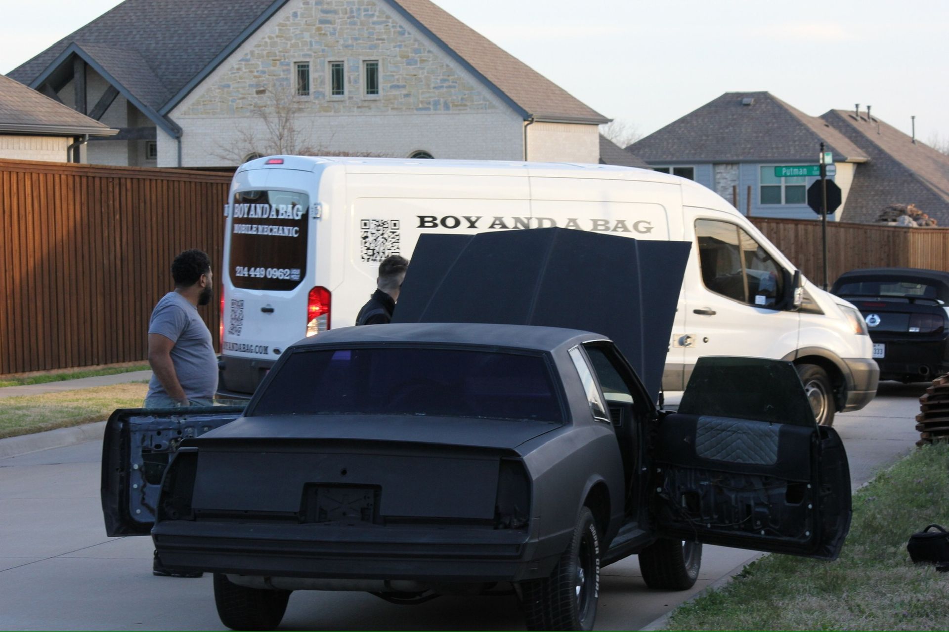 Two men loading a black truck bed into a white moving van in a suburban driveway.