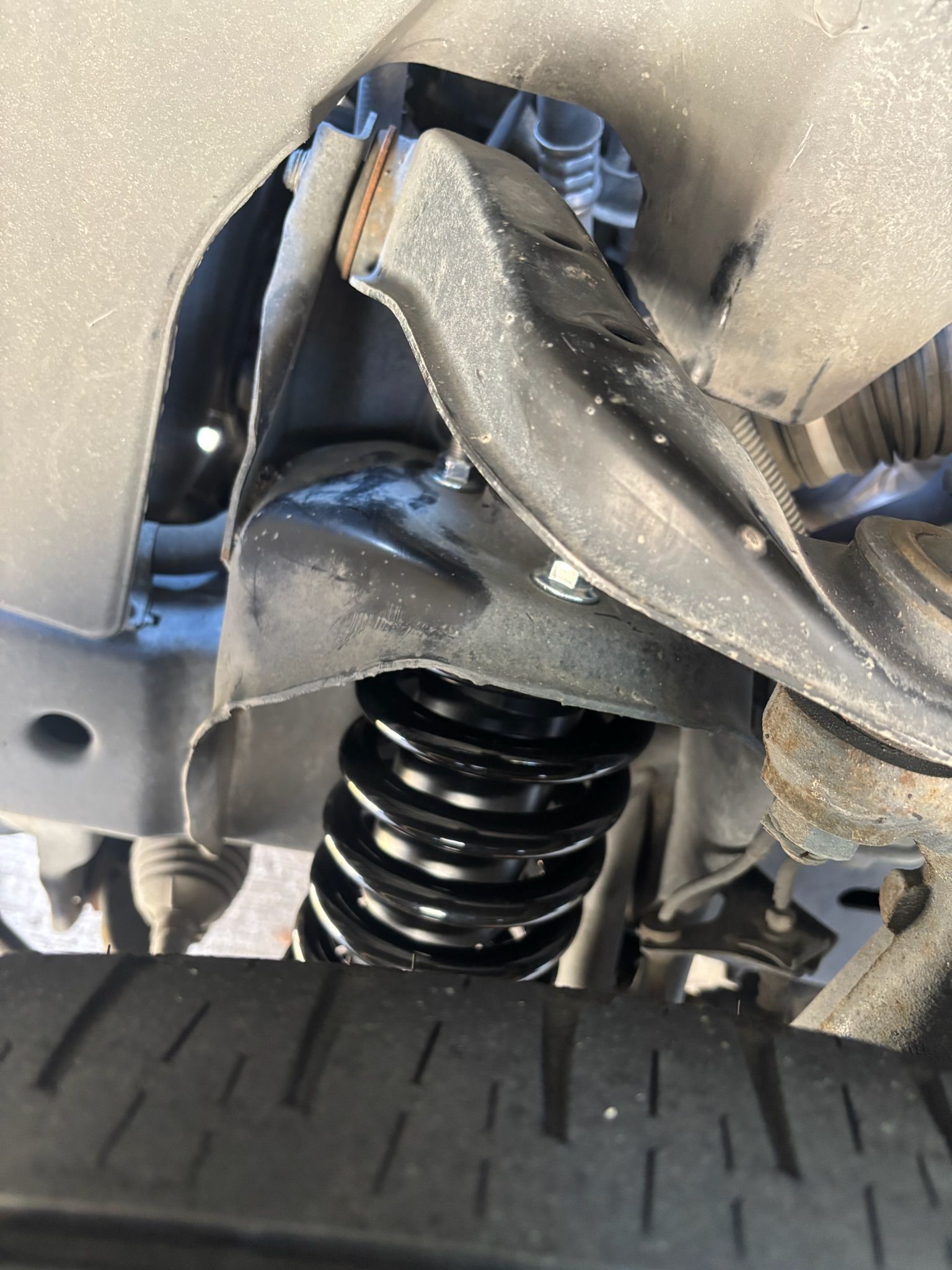Close-up of a car’s damaged wheel well, exposed suspension spring, and torn inner fender lining