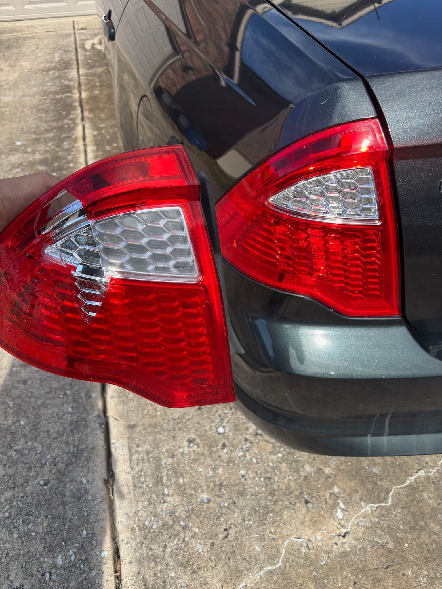 Broken red car taillight hanging off the rear of a dark sedan
