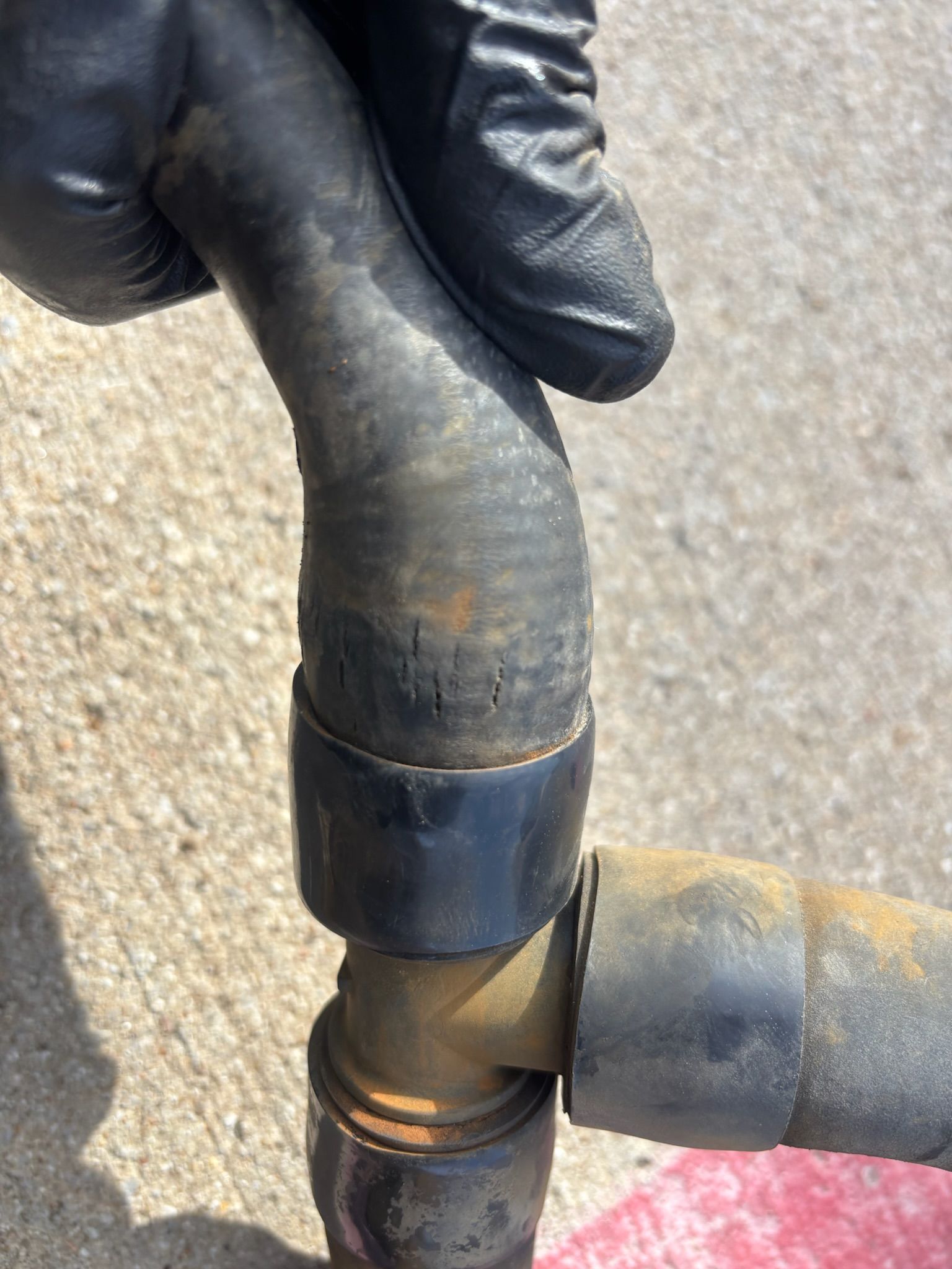 Gloved hand holding a black rubber hose connector with a brass fitting.
