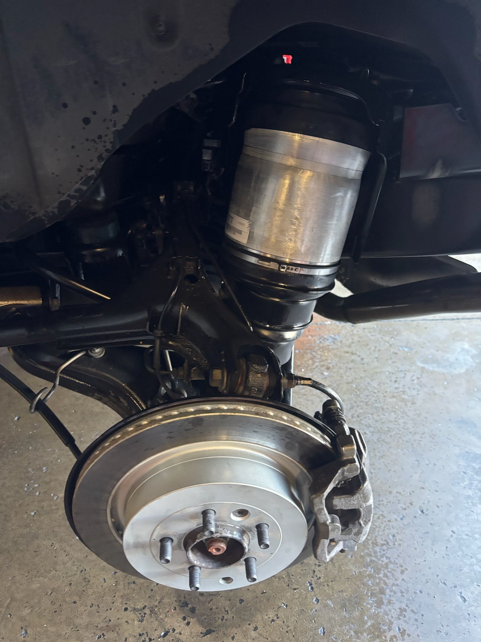Car wheel and brake assembly in a dark vehicle wheel well, with the suspension visible.