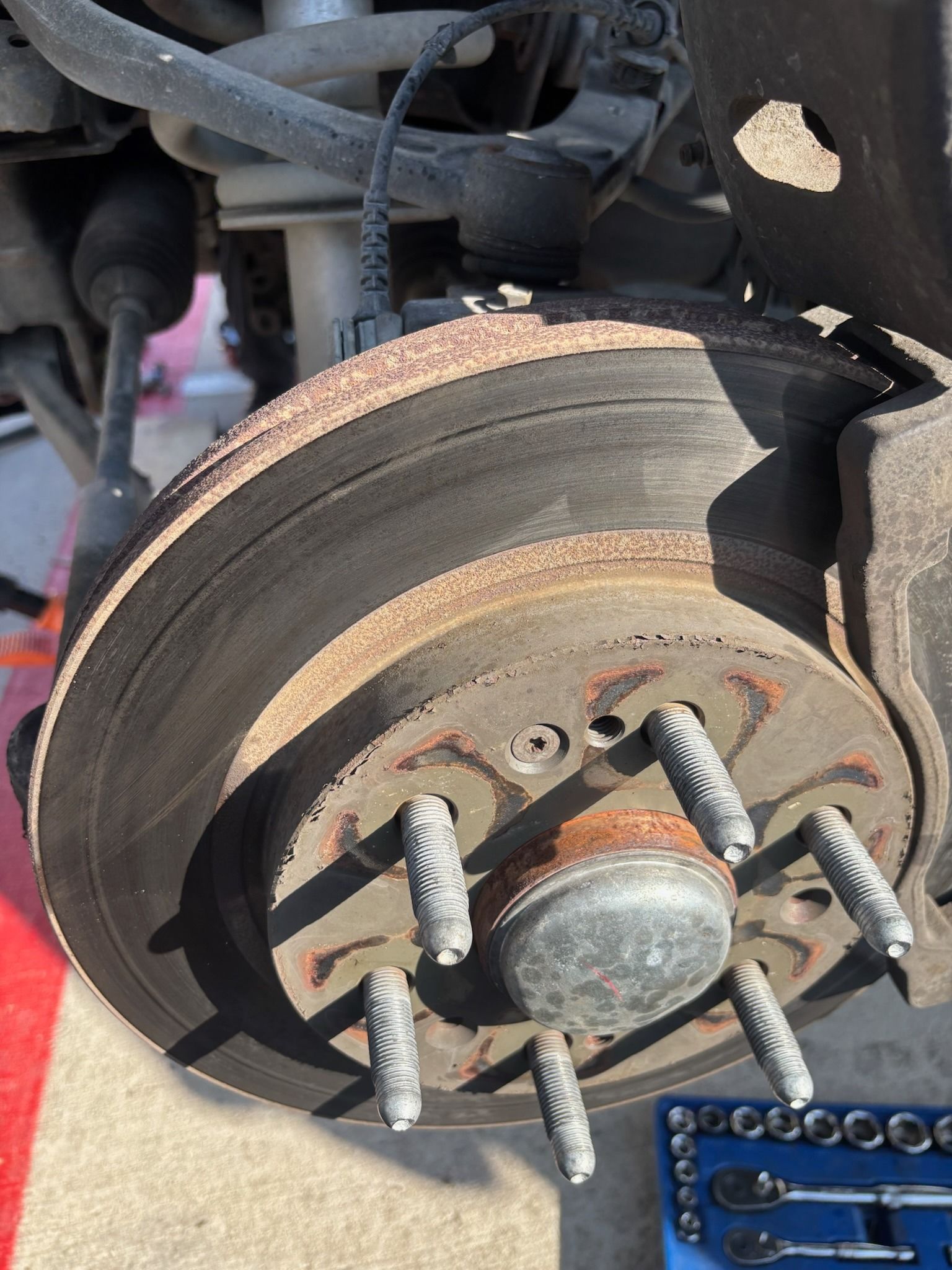 Close-up of a car brake rotor and hub with lug studs, showing rust and wear.