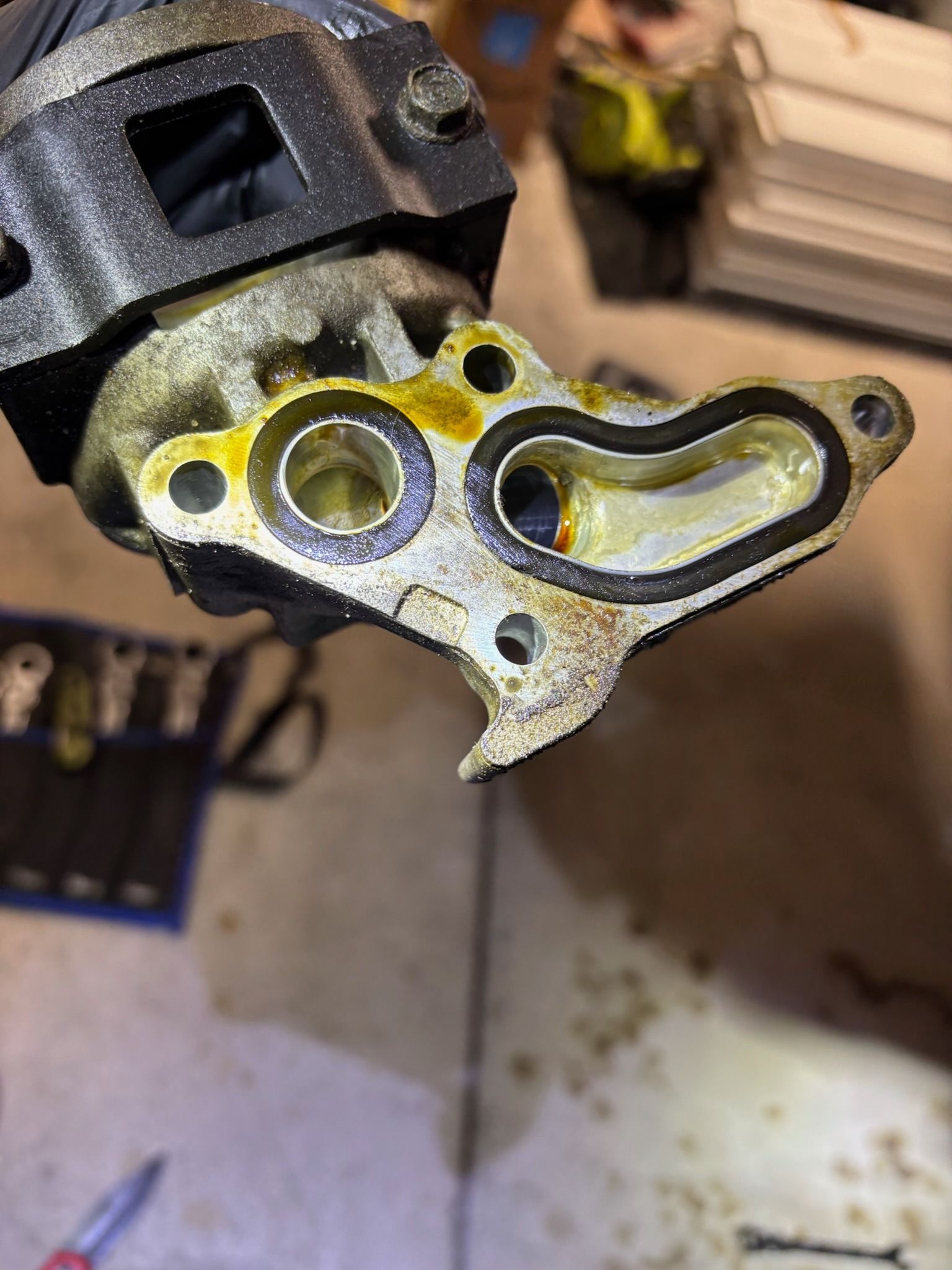 Close-up of a greasy metal engine part with bolt holes and a gasket outline on a workbench