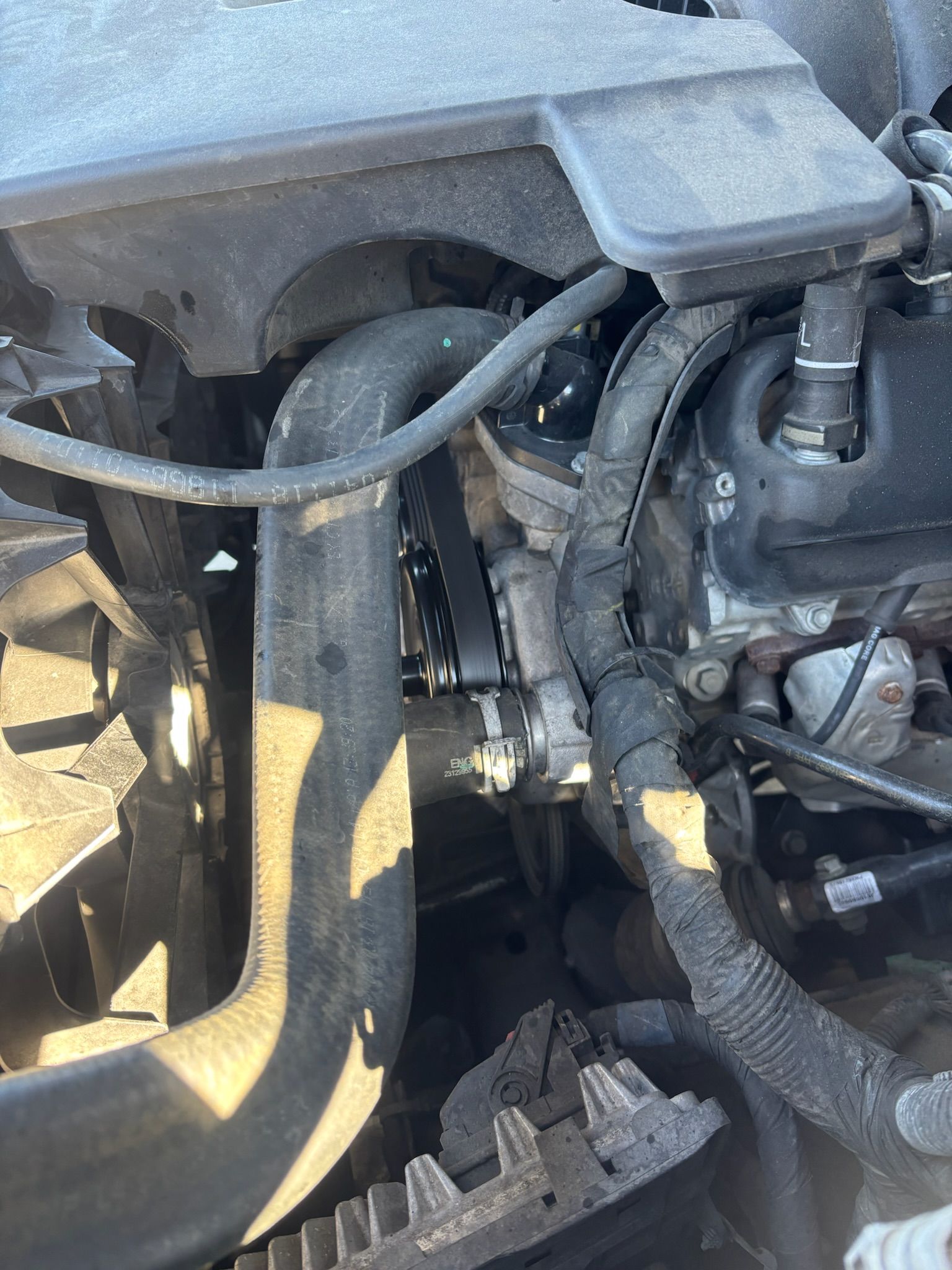 Close-up of a dusty car engine bay with hoses, wiring, and mechanical components.
