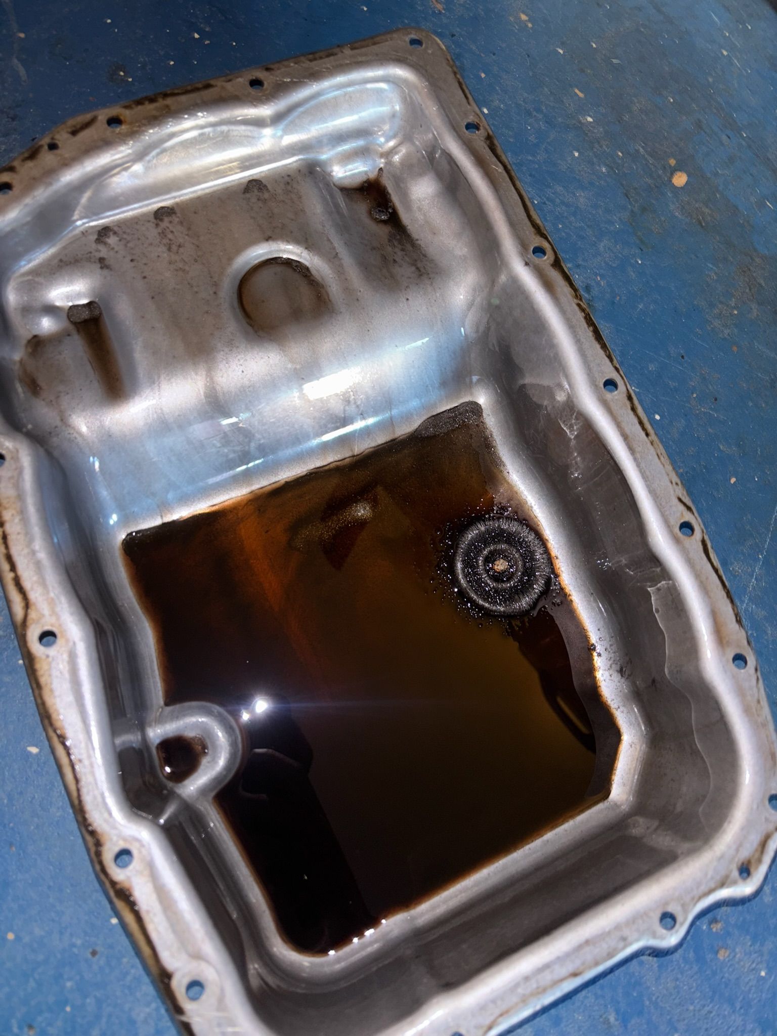 Shiny metal oil pan with dark fluid pooled inside on a blue floor