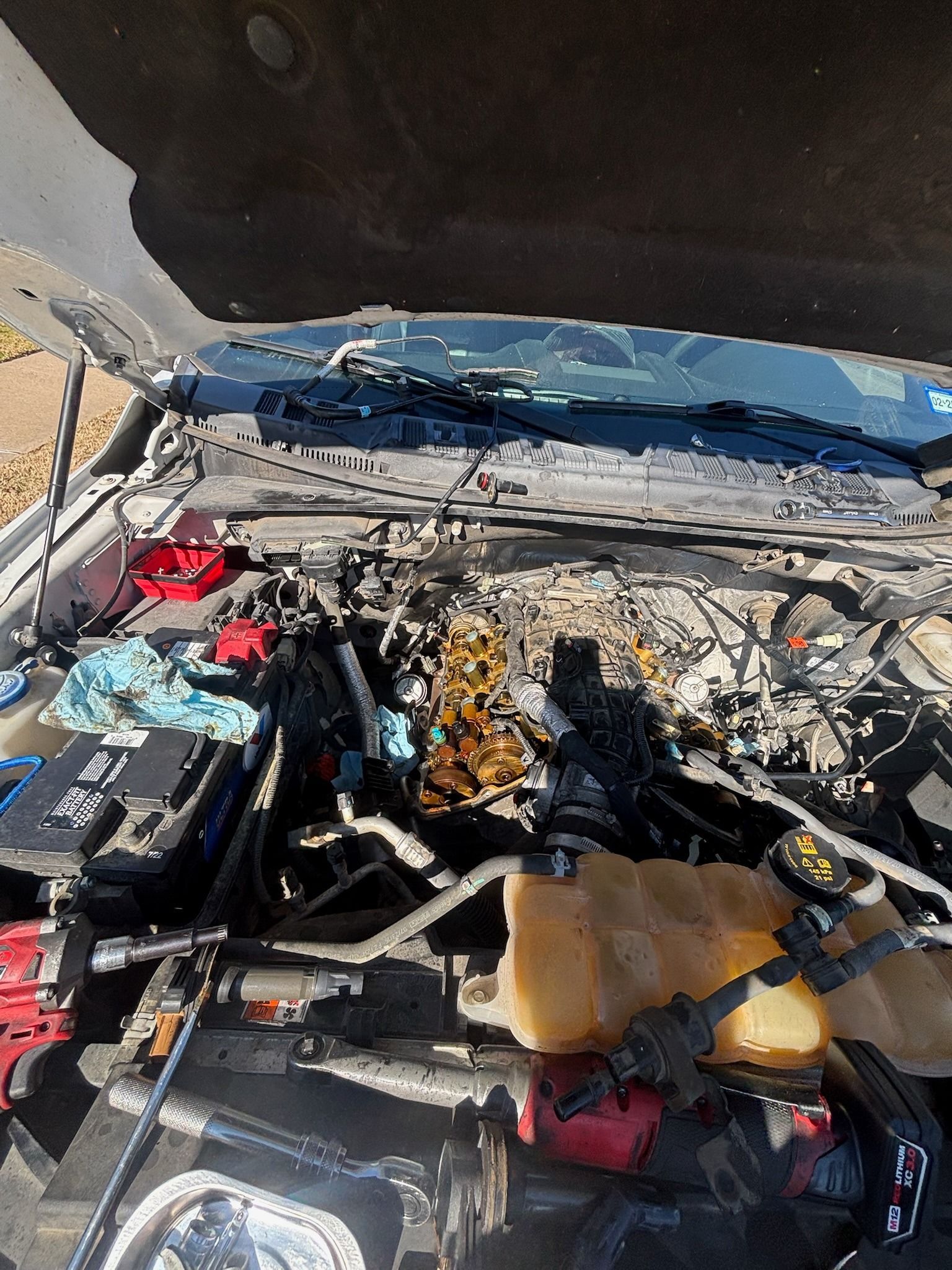 Car engine bay with the hood open, showing exposed components and damaged wiring.