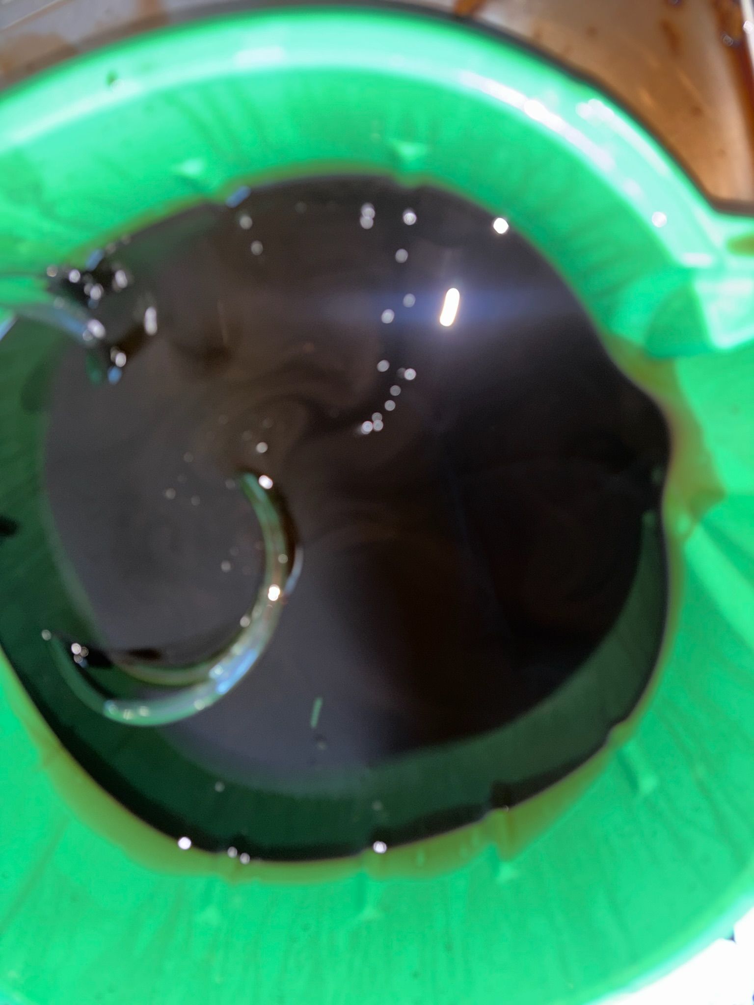 Dark liquid in a green plastic bucket with a metal chain submerged inside.