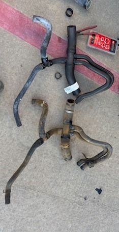 Assorted bent metal pipes and hoses laid on concrete, with a red digital display near the top right.