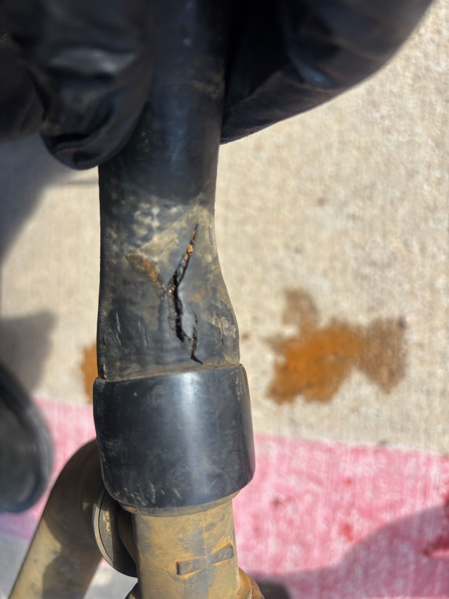 Gloved hand holding a cracked black cable or hose with exposed damage near a connector, outdoors on concrete.