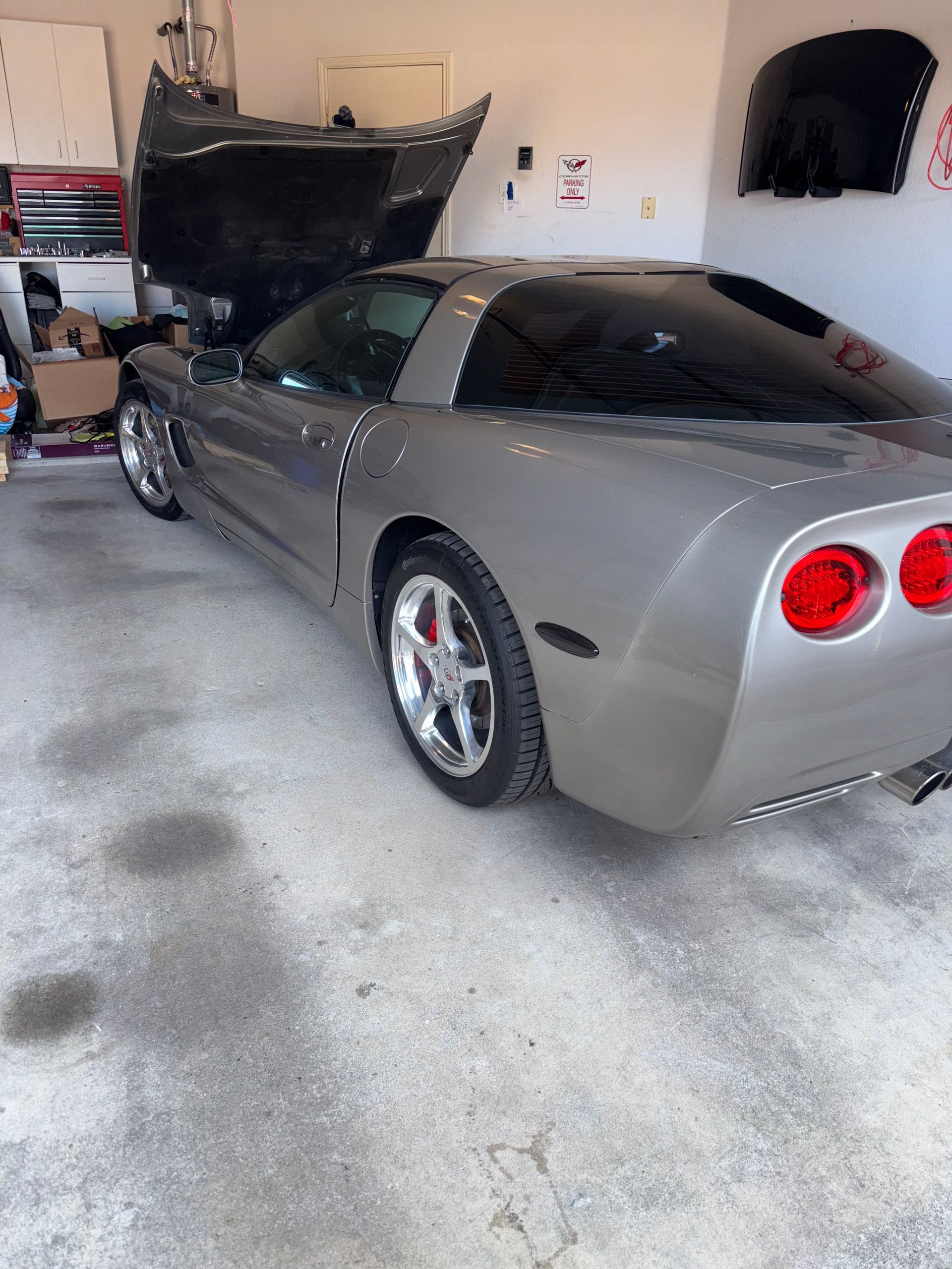 Gray sports car parked in a garage with its hood open and rear lights visible