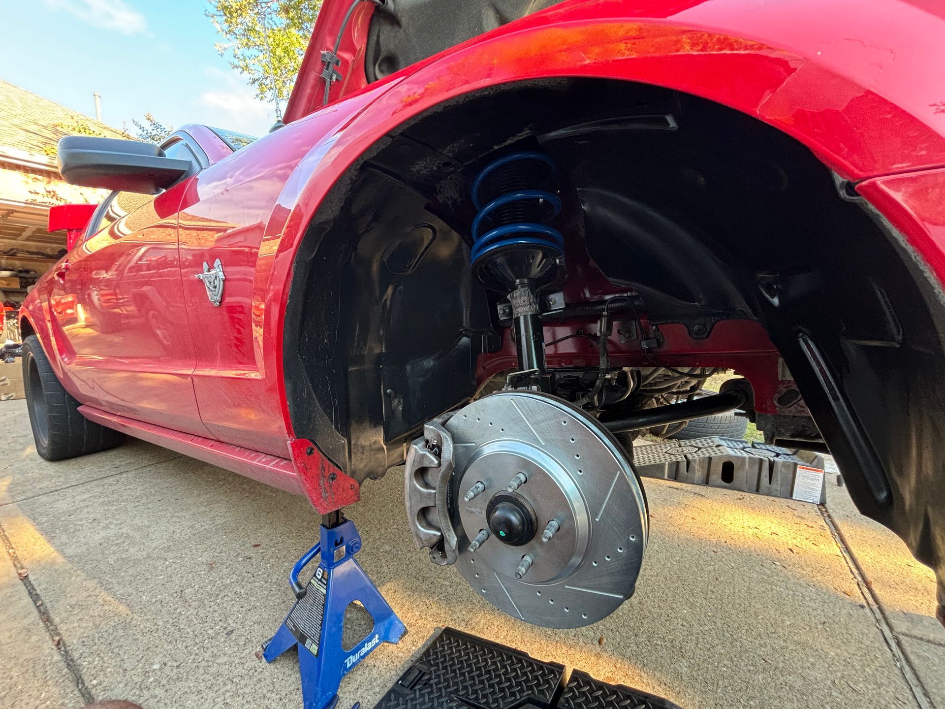 Red sports car on jack stand with front wheel removed, exposing brake disc and suspension.