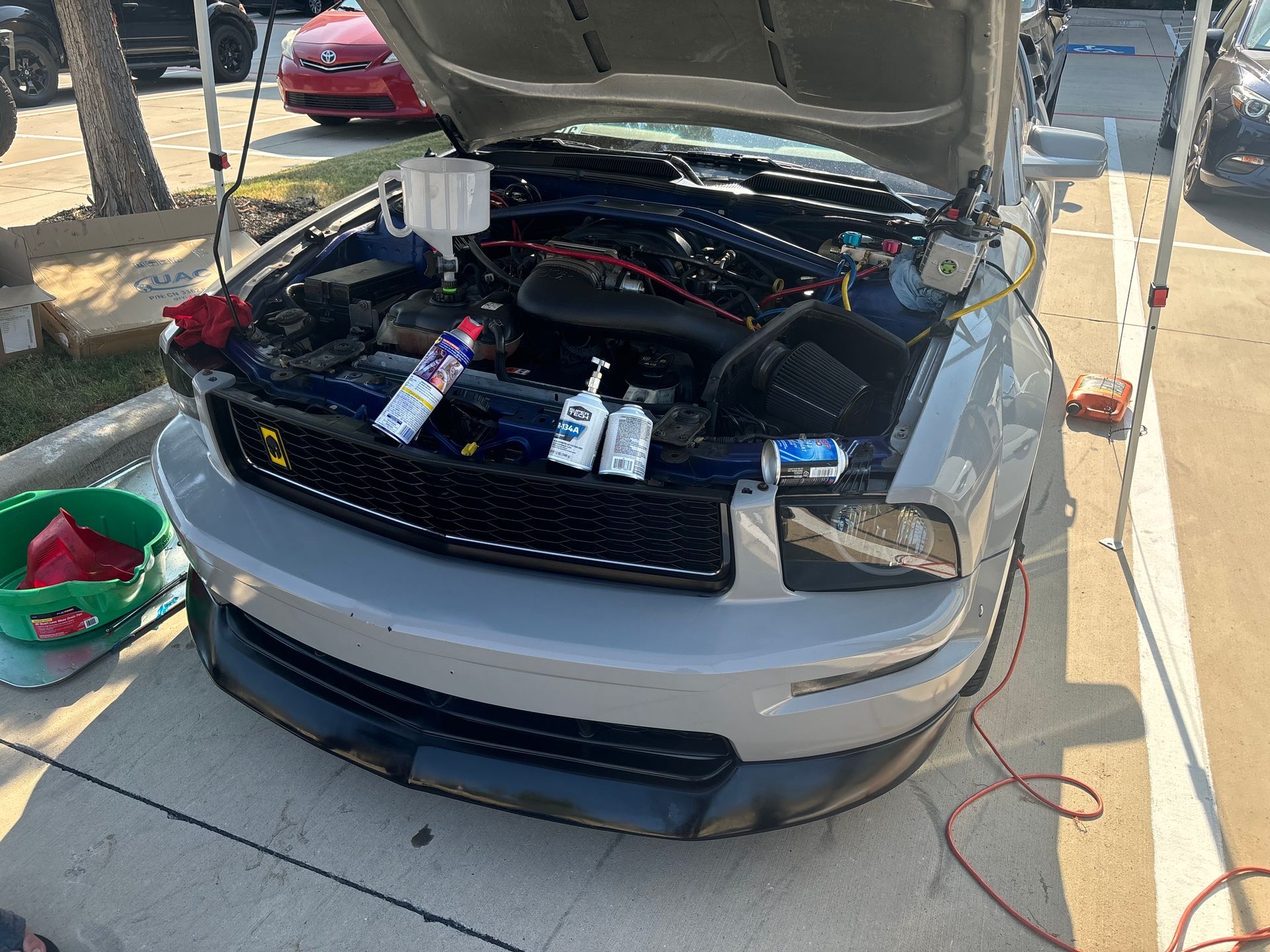 Car with hood open in a driveway, engine bay exposed and tools nearby for maintenance