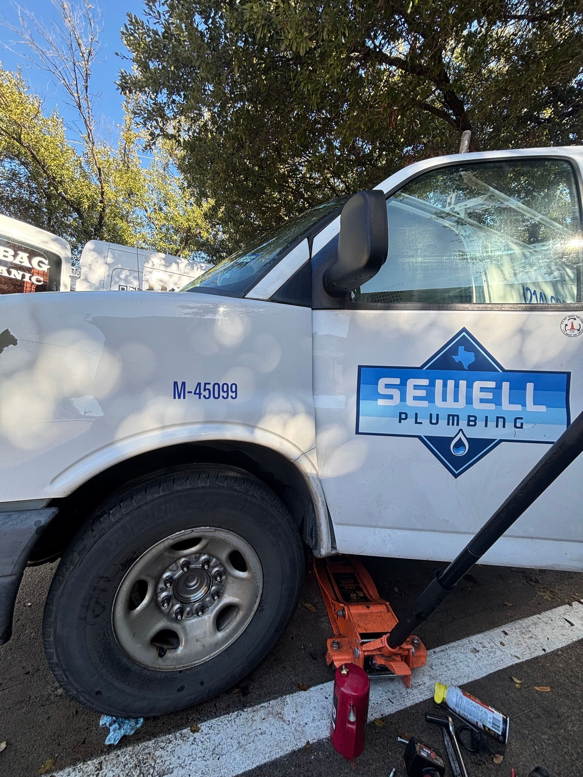 White Seibell Plumbing truck with shattered windshield, parked outdoors with tools on the ground.