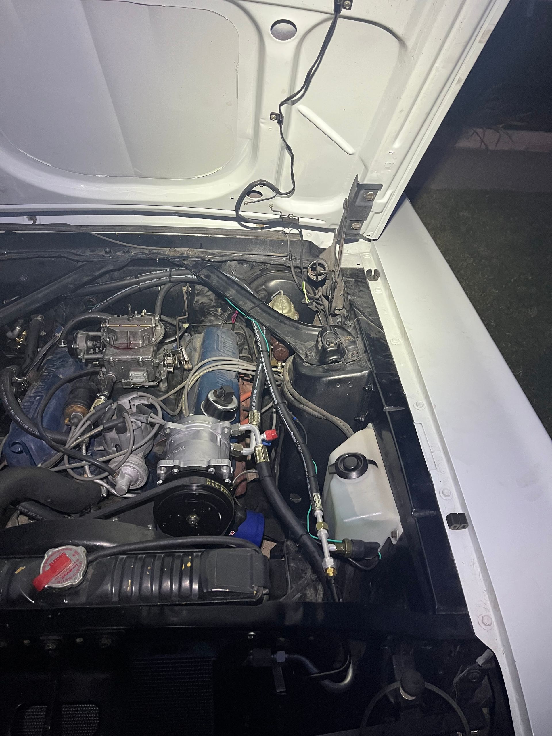 Open car hood showing a cluttered engine bay with exposed wiring and mechanical components.