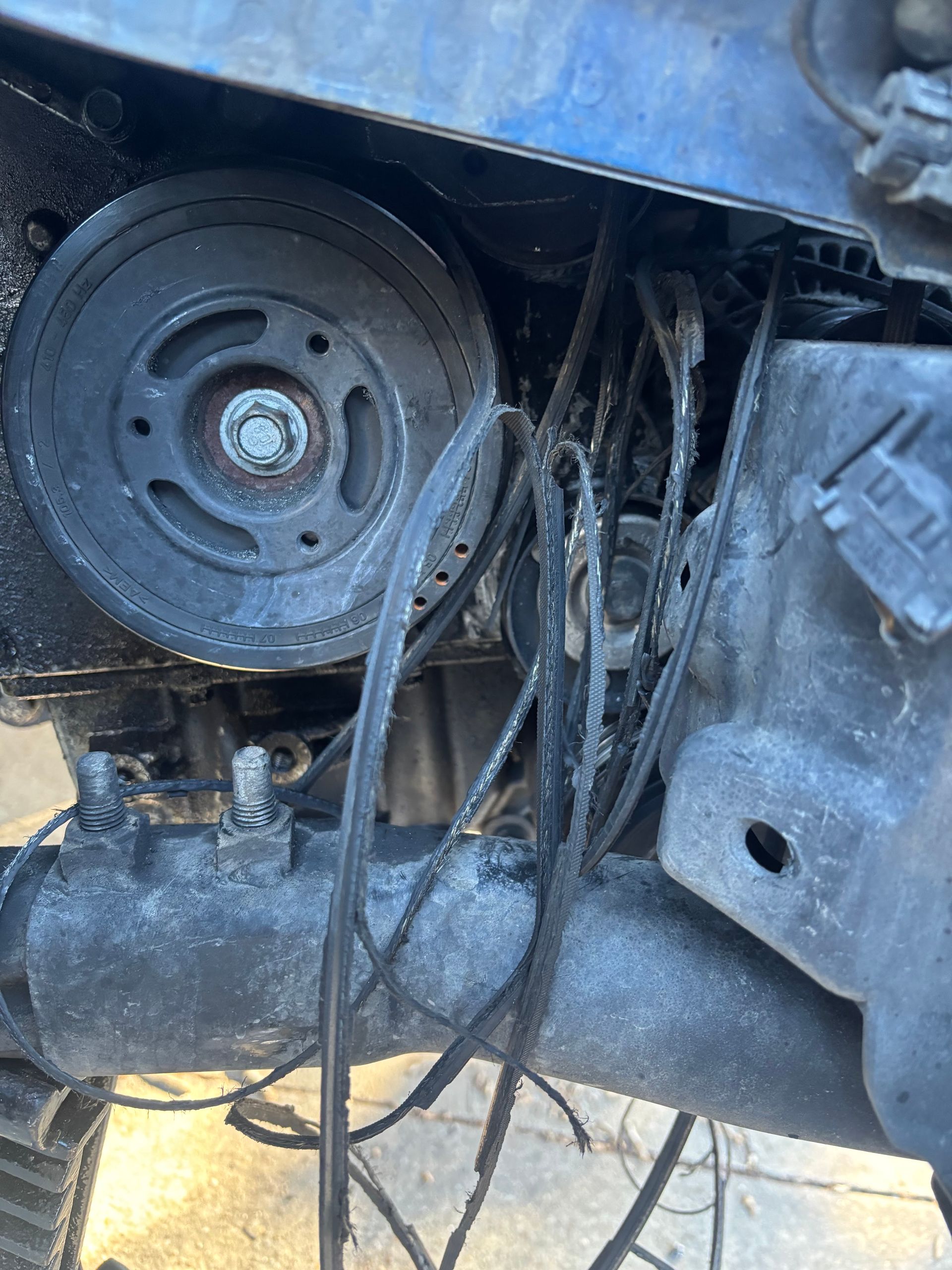 Close-up of an exposed car engine pulley with hanging wires and a blue metal frame