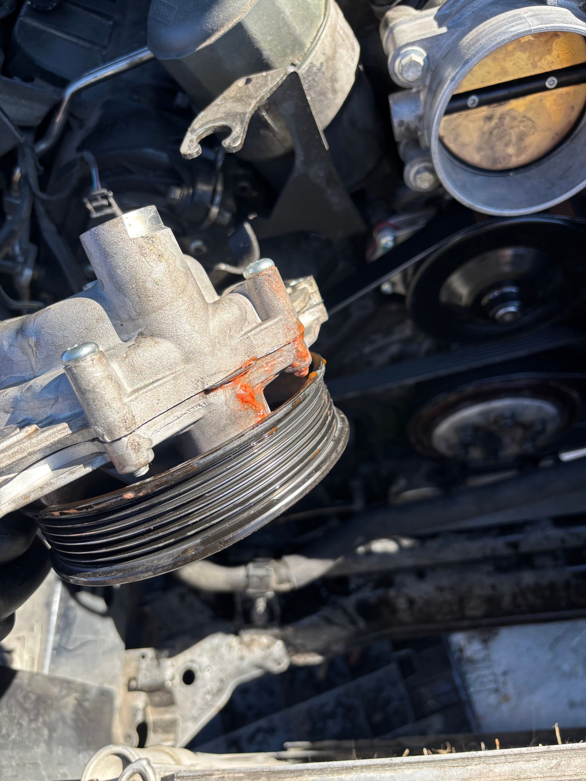 Close-up of a worn car belt pulley and engine components with orange rust and dirt buildup