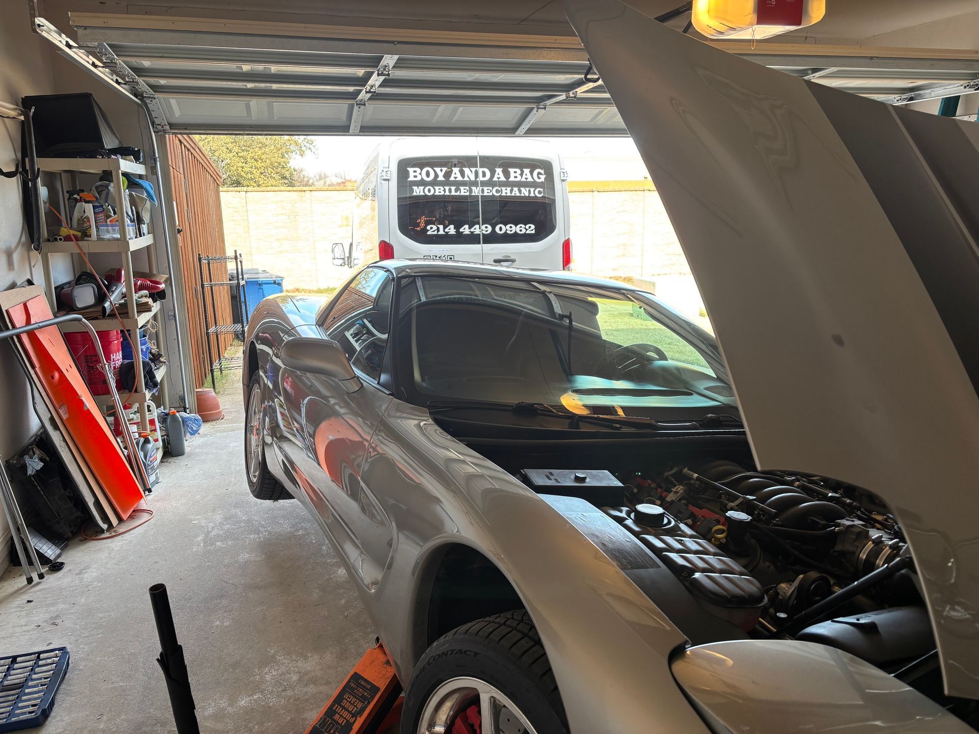 Silver car parked in a cluttered garage with its hood open and engine exposed